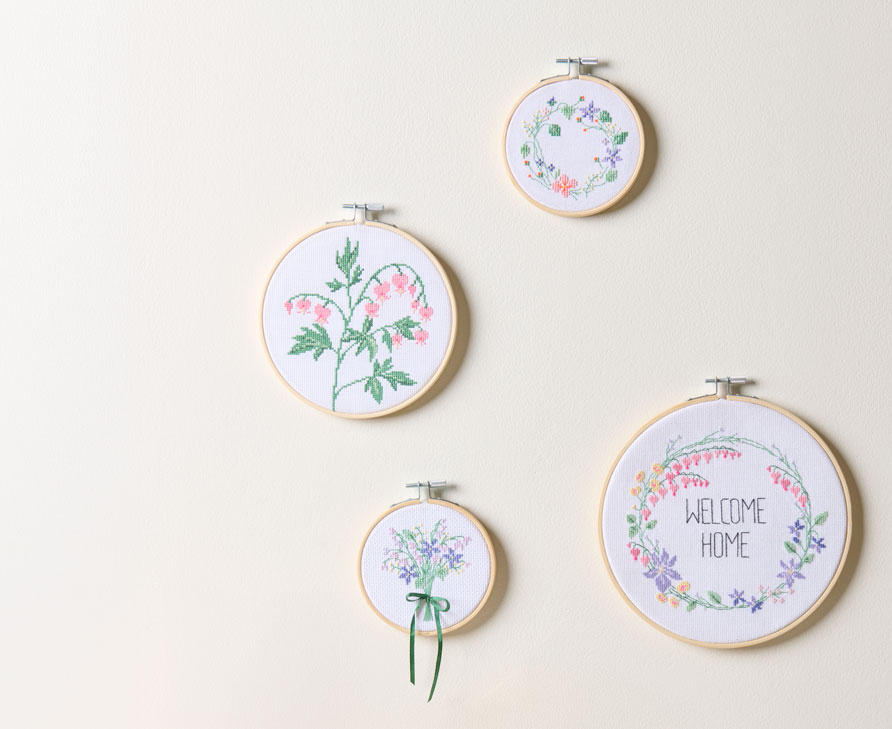 4 blumige Stickbilder im Stickrahmen hängen an einer Wand