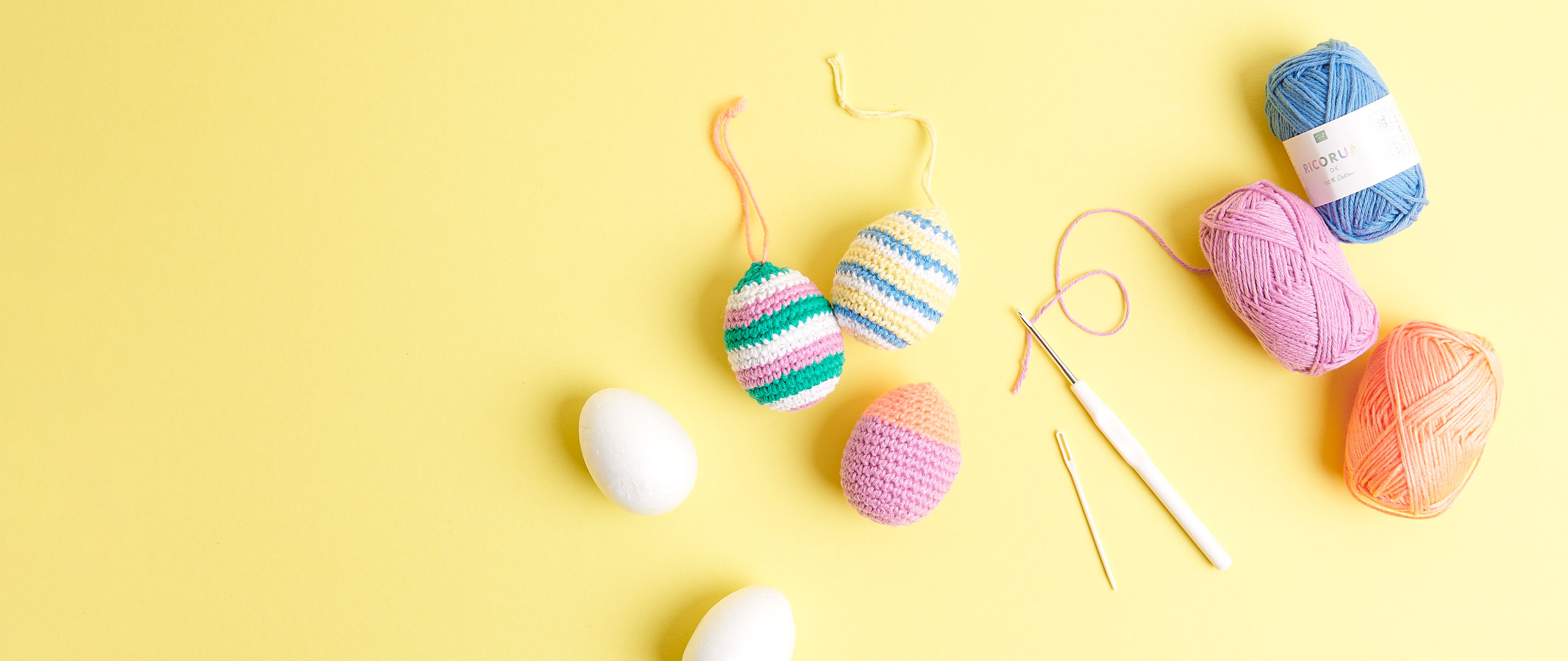 Gehäkelte Ostereier liegen auf gelbem Untergrund