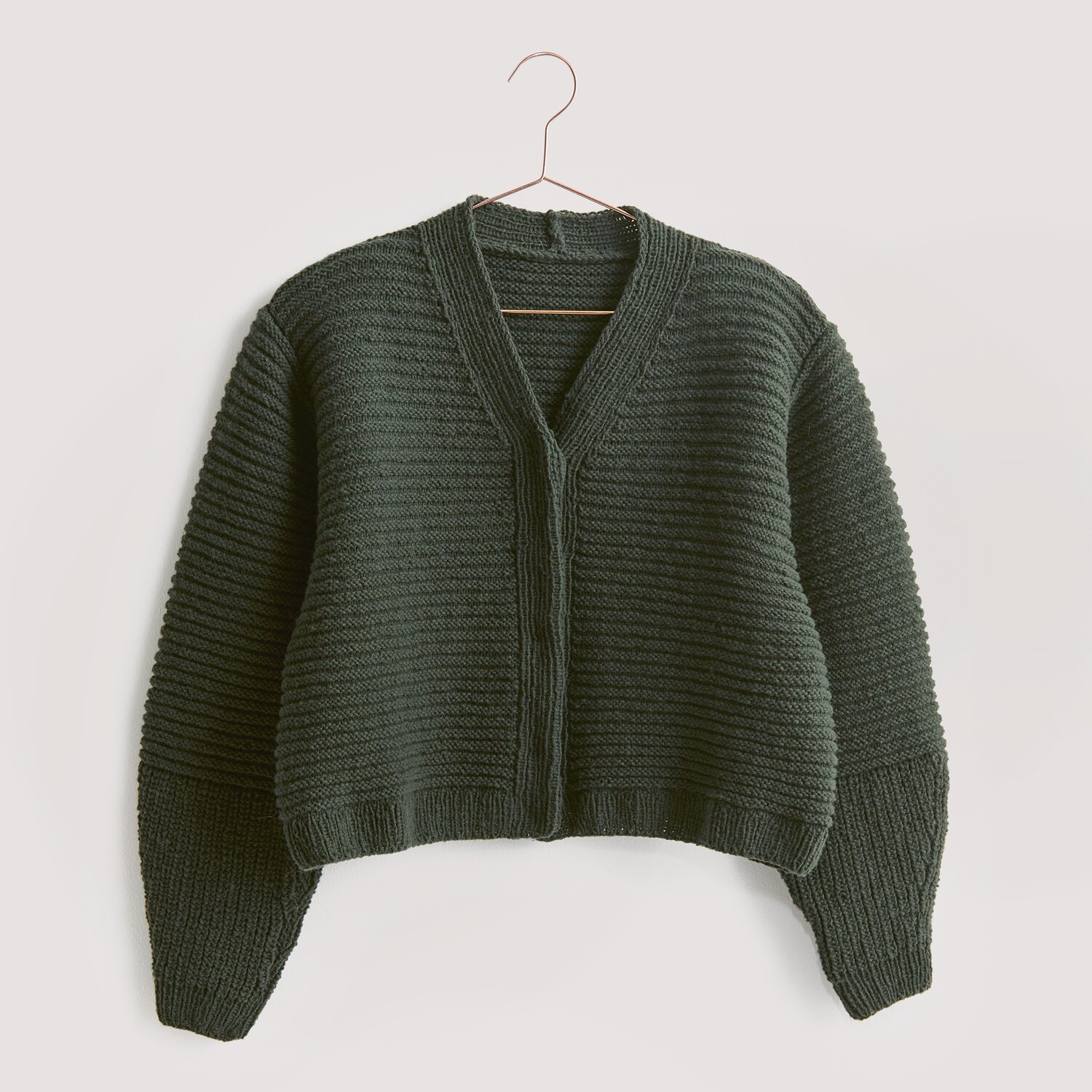 Strickset Jacke Modell 16 aus Luxury Knits, dunkelgrün, aus Premium Natural Fibres, auf einem Kleiderbügel.