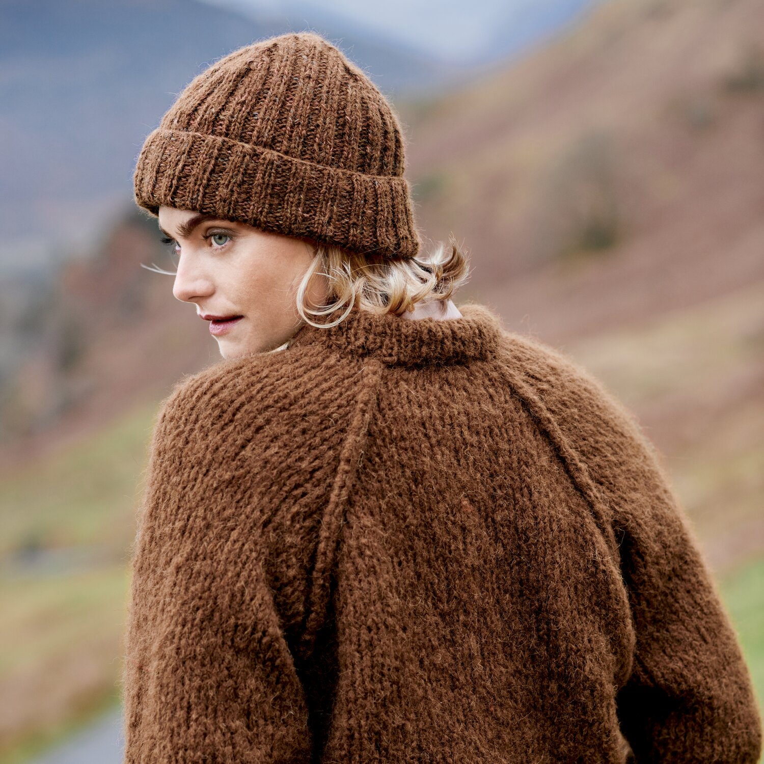Strickset Mütze Modell 16b aus Lovewool No. 23, gestrickte Beanie und passender Pullover aus weichem Garn, getragen von Frau in herbstlicher Berglandschaft