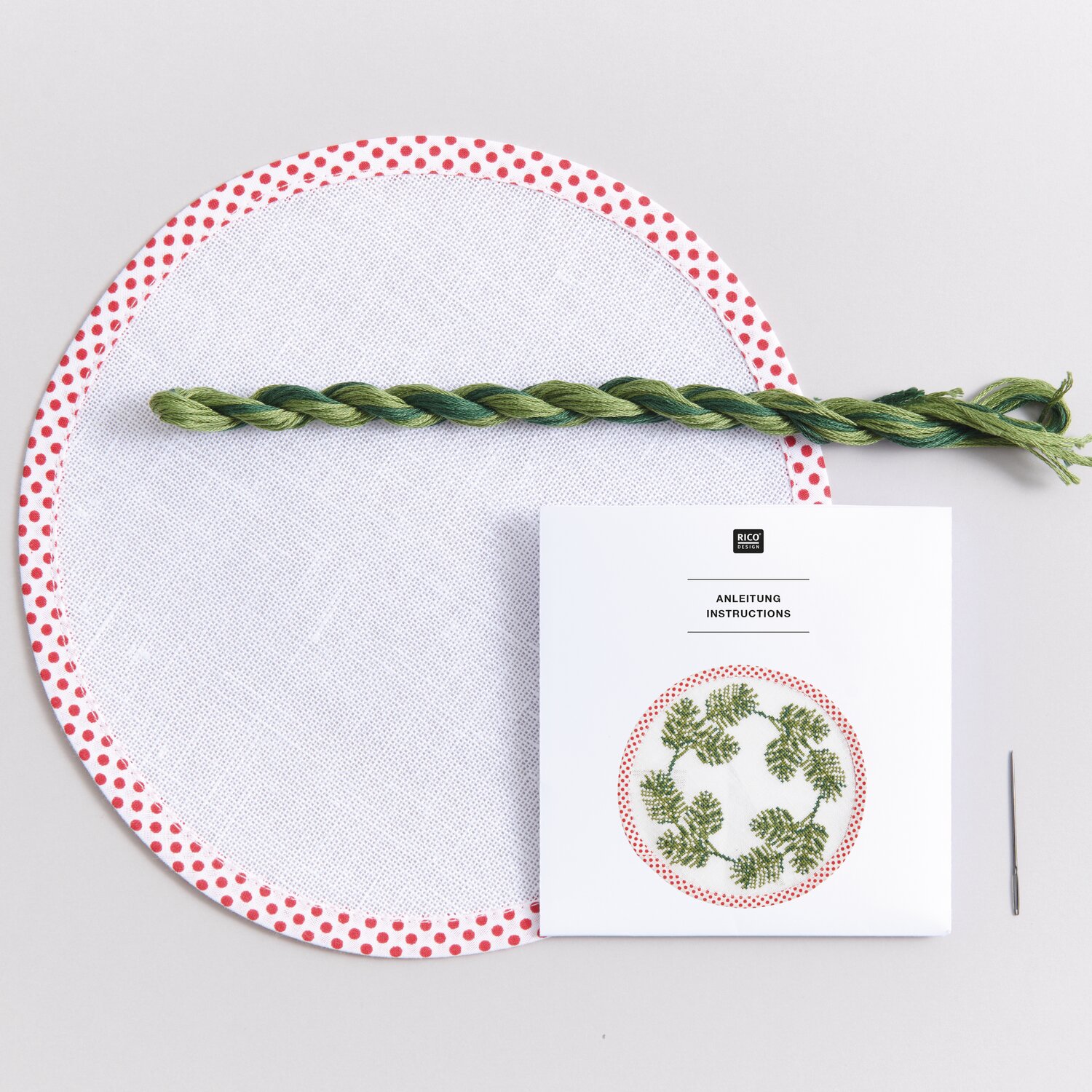 Stickpackung Untersetzer rund Tannenzweige mit grünem Garn, Anleitung und Nadel auf weißem Hintergrund.