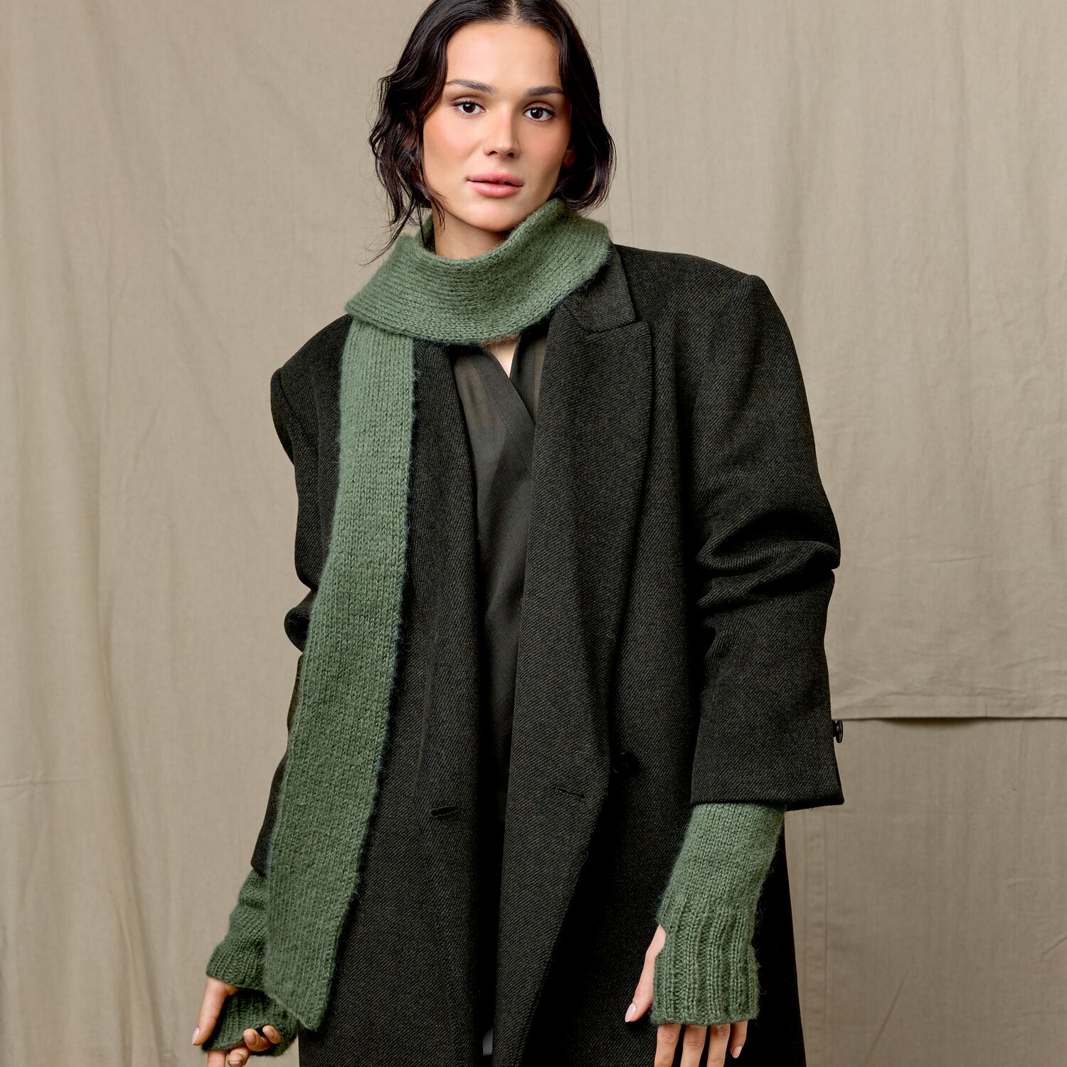 Strickset Minischal 05 aus Luxury Knits Little Pieces, langer Schal mit passenden Armstulpen in Grün, getragen zu dunklem Mantel vor einfarbigem Hintergrund