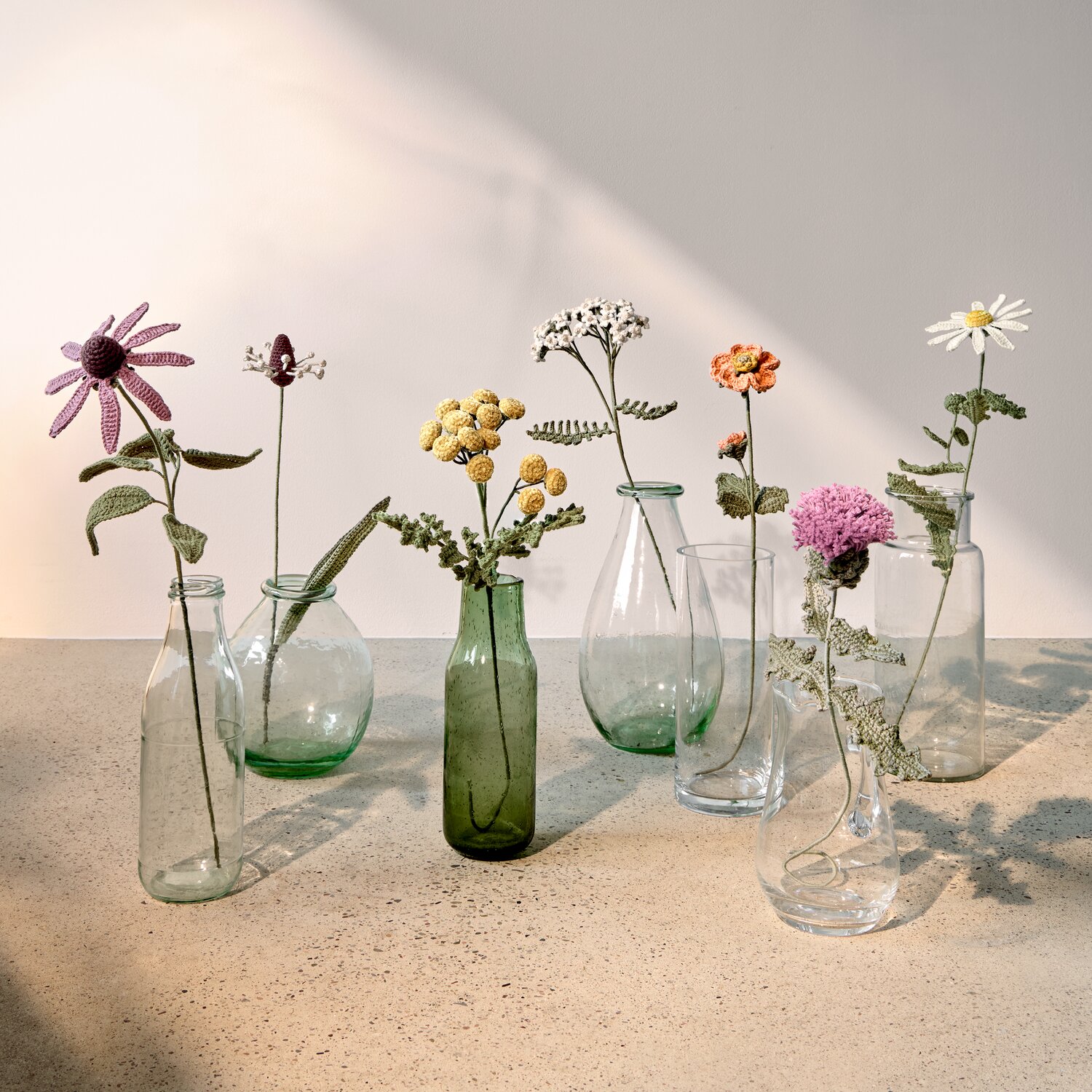 Ricorumi In the Meadow zeigt gehäkelte Blumensträuße aus Creative Ricorumi dk in bunten Naturtönen, dekoriert in durchsichtigen Glasvasen auf heller Steinoberfläche, 25g