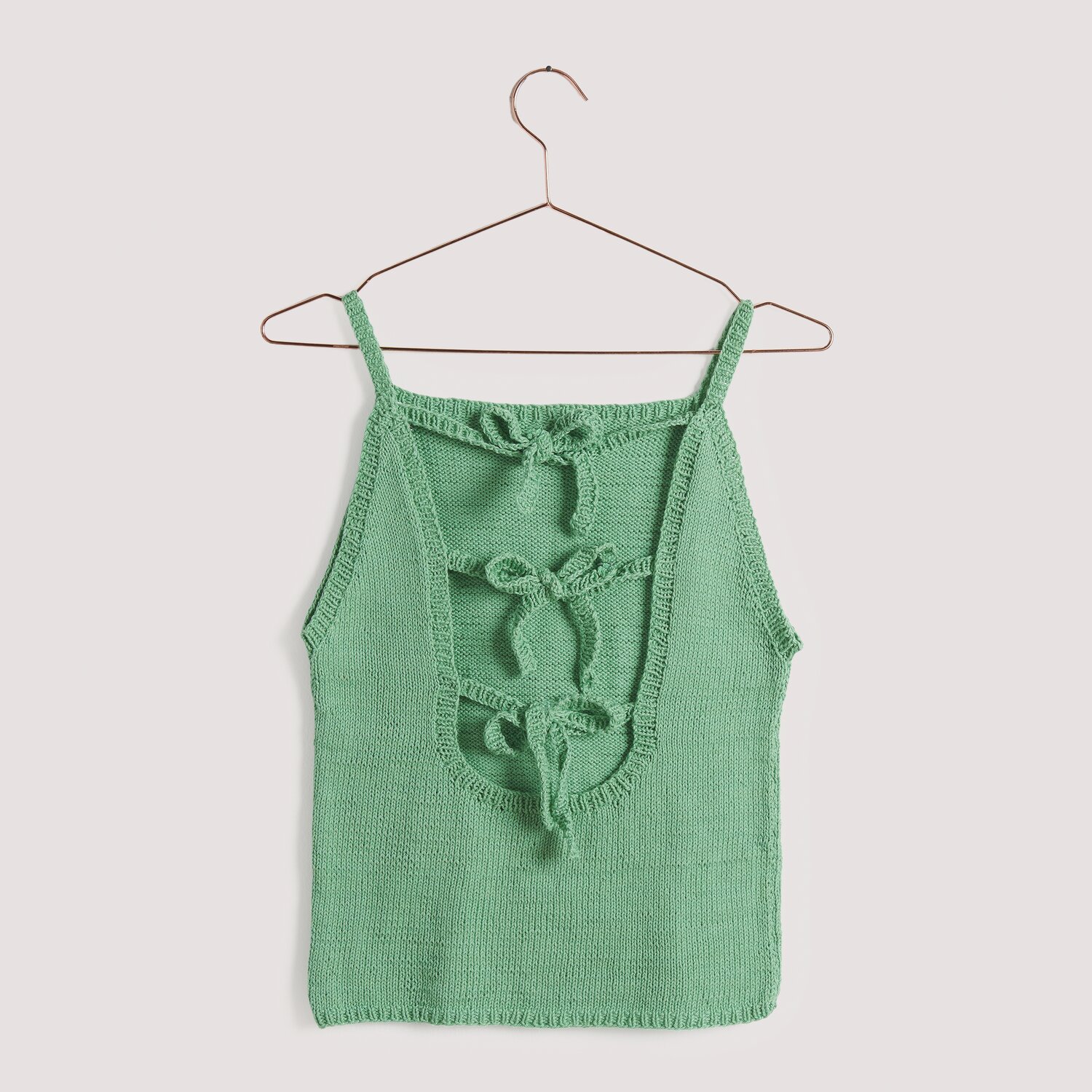 Rico Cotton: Grünes Stricktop mit Schleifen-Details, präsentiert auf einem Kleiderbügel. Ideal für Frühjahr-Sommer.