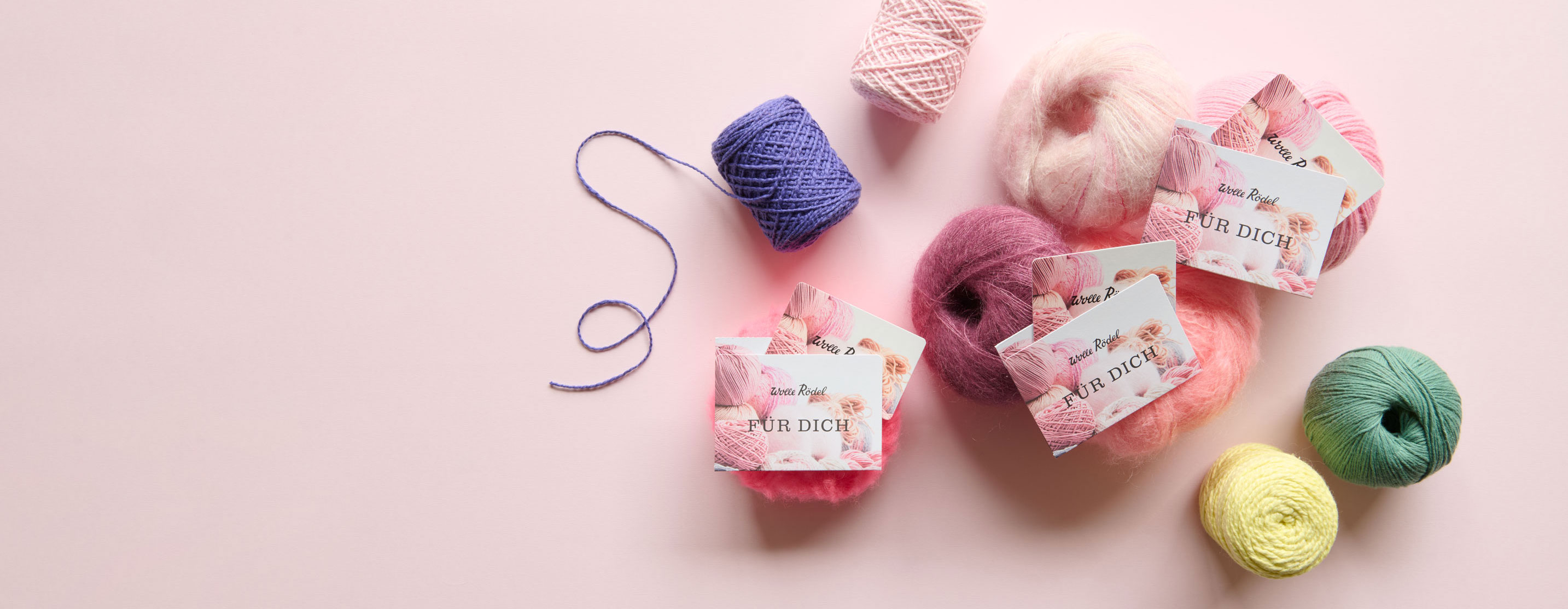 3 Wolle Rödel Geschenk-Karten liegen auf bunten Wollknäuel