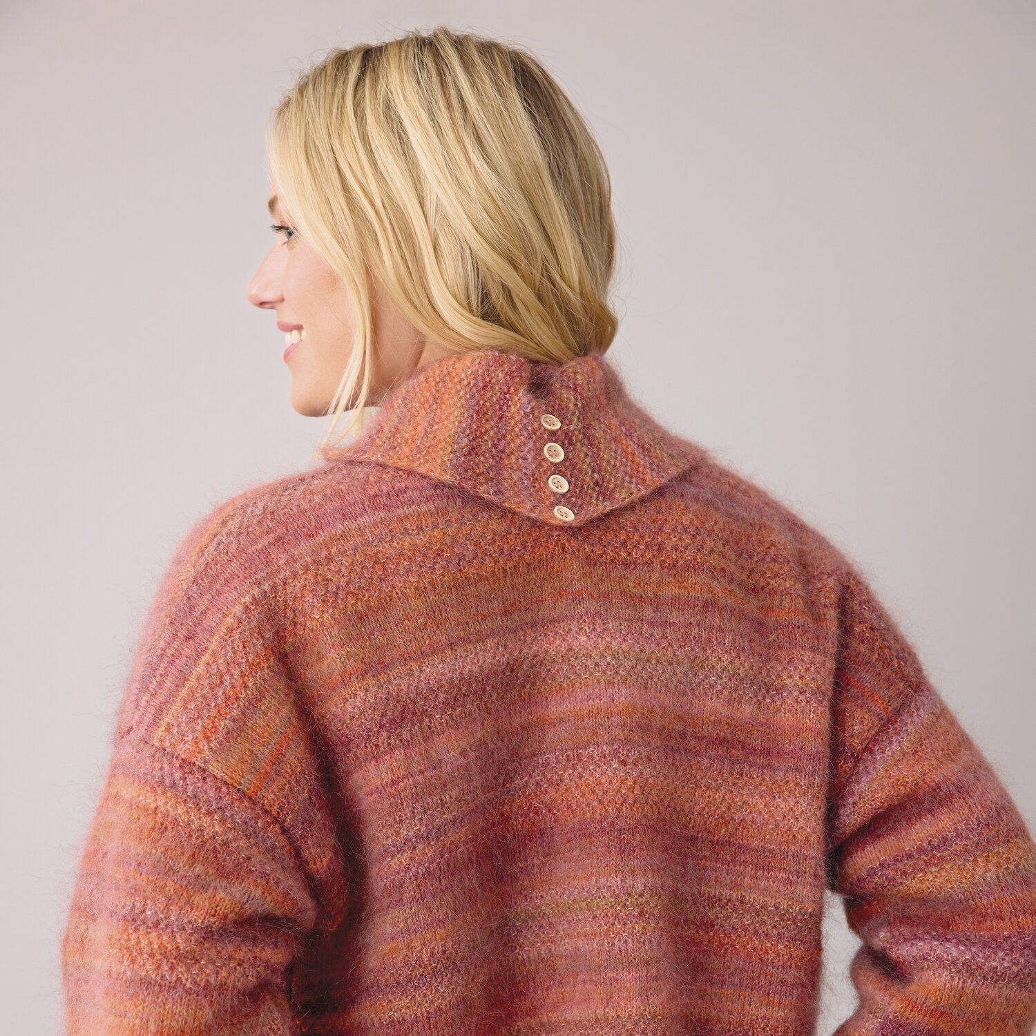 Strickset Schal mit Schlaufen Modell 02 aus DNM 14. Frau trägt gestrickten Pullover in warmen Rottönen mit Knöpfen am Kragen.