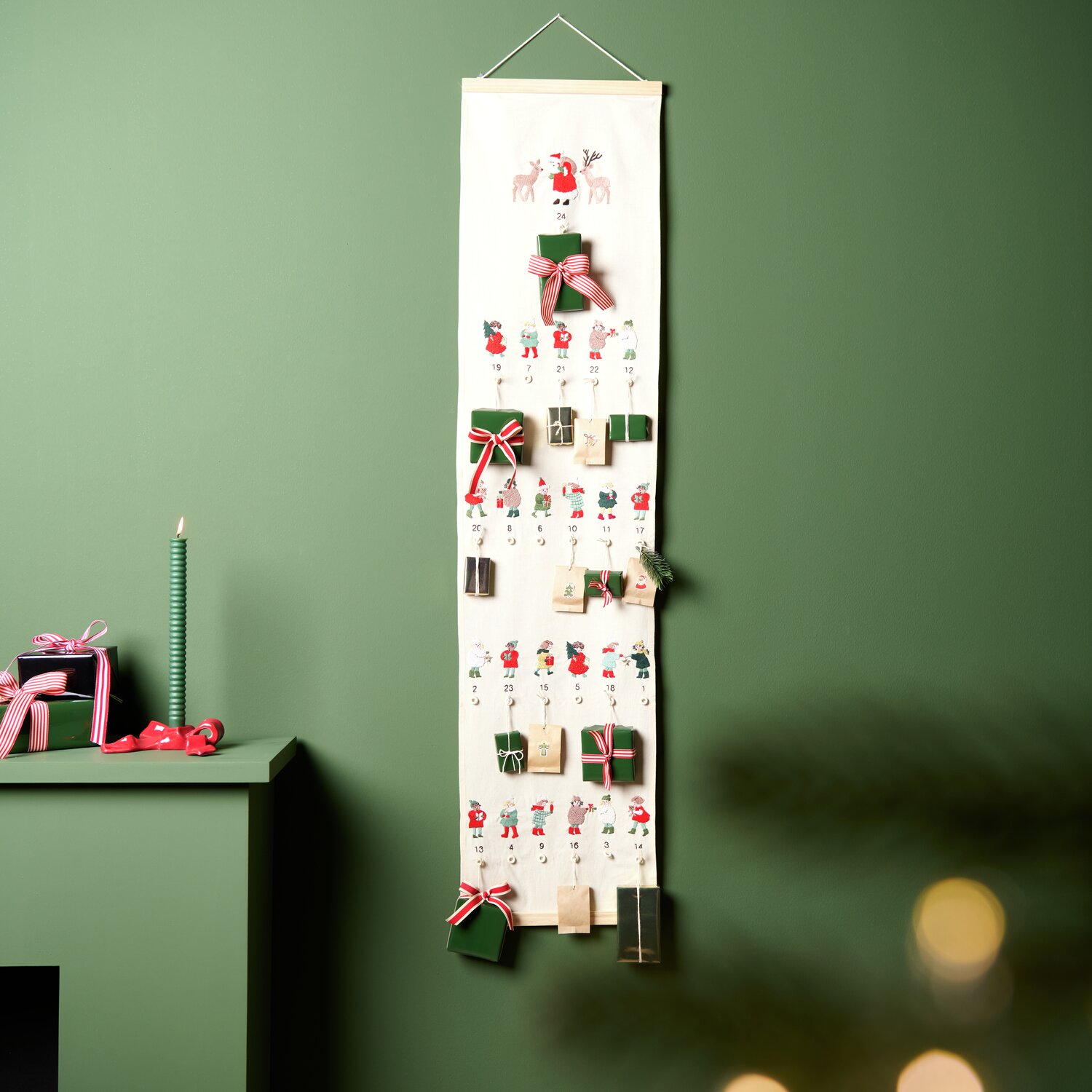 Stickpackung Adventskalender Kinder vorgezeichnet: Ein dekorativer Adventskalender mit kleinen Geschenken und weihnachtlichen Motiven an einer grünen Wand.