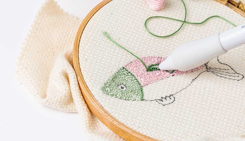 Anleitung Weihnachtliche Punch Needle Anhänger: Stickrahmen mit Fischmotiv in Grün und Rosa, verziert mit Punch Needle Werkzeug.