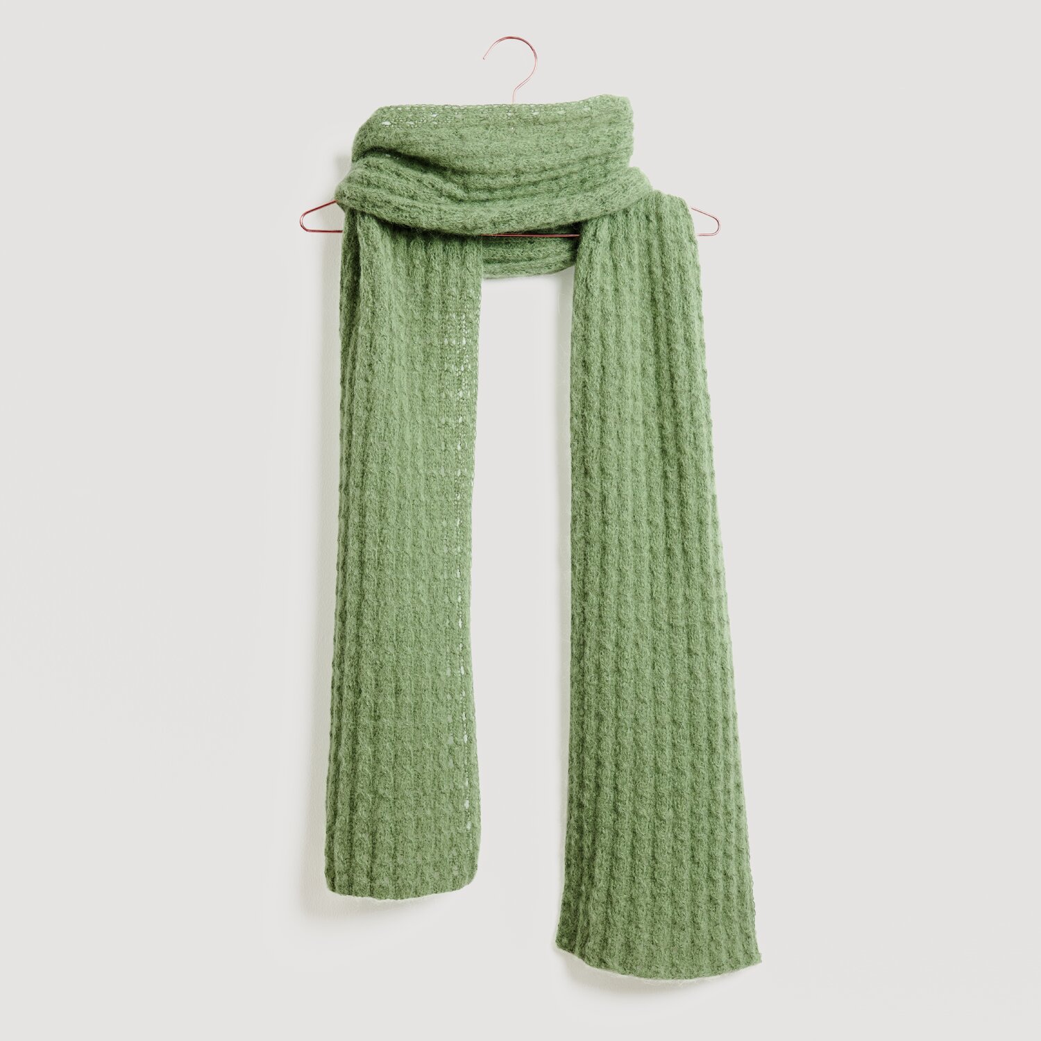 Grüner Schal von Modell Legeware, elegant drapiert auf einem Haken. Der Schal hat eine strukturierte Oberfläche und bietet stilvolle Wärme für kalte Tage. Ideal für modische Akzente.