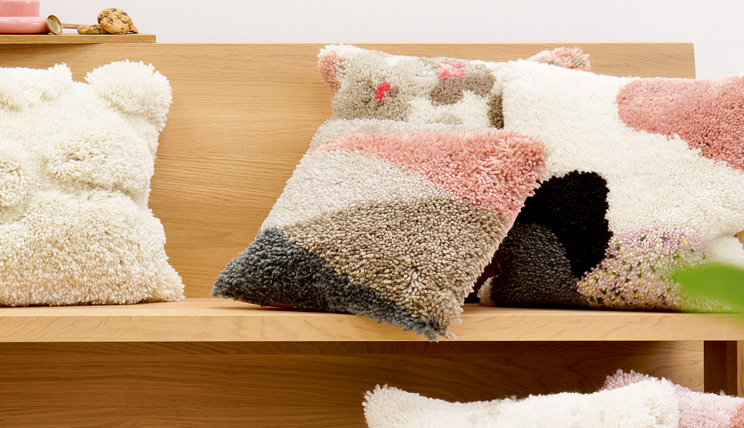 Anleitung Knüpfen Kissen mit Dreiecksmuster: Flauschige Kissen in Rosa, Beige und Schwarz auf Holzbank.