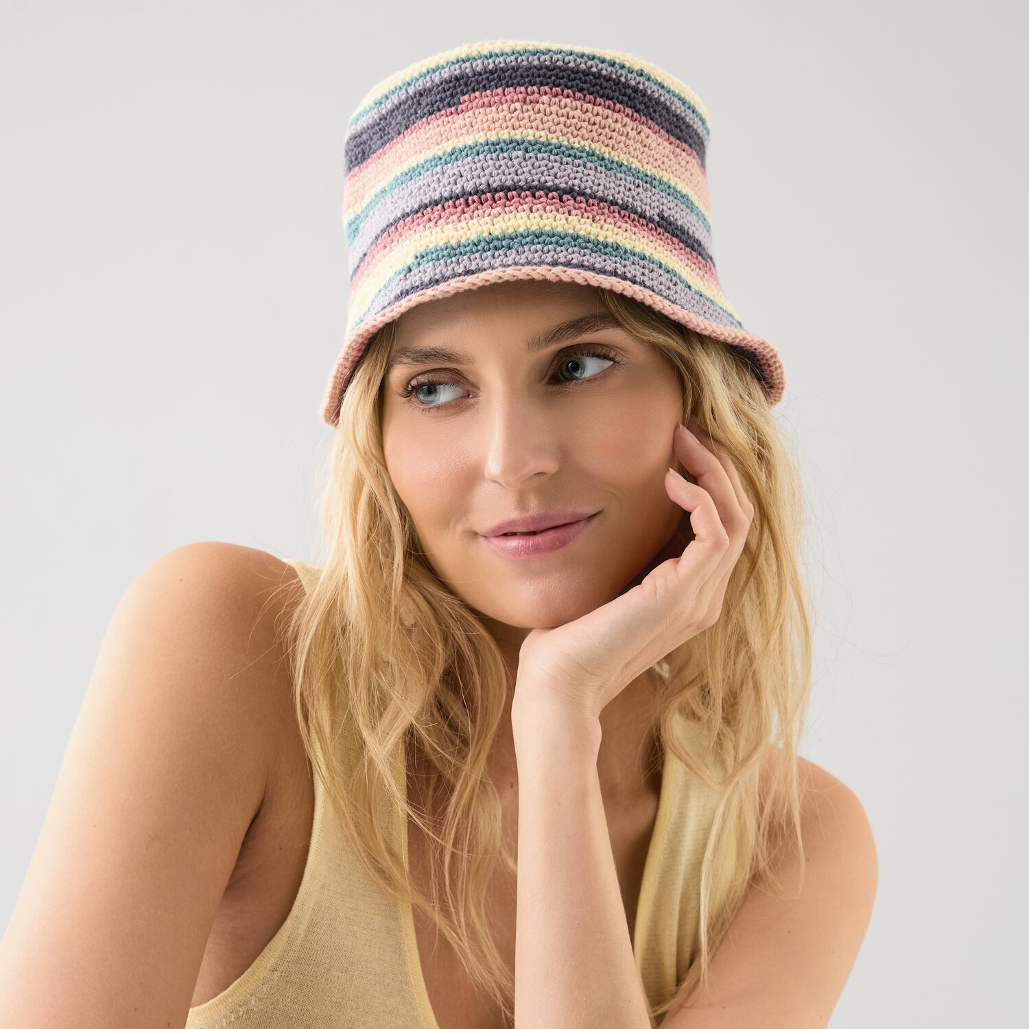 Häkelset Bucket Hat Modell 08: Frau trägt pastellfarbenen, gestreiften Hut aus Die Neue Masche No. 15.