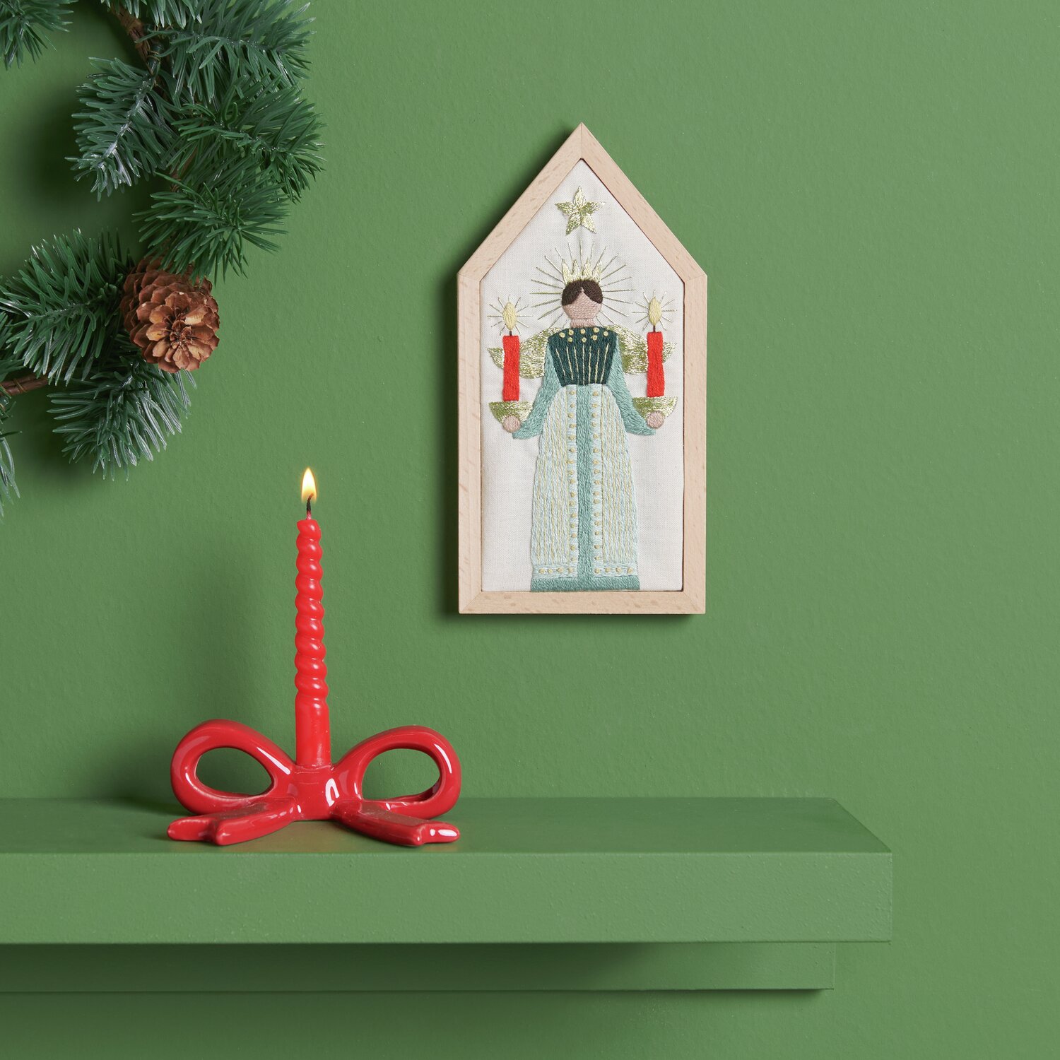 Stickpackung Engel vorgezeichnet 9x18cm von Rico Design Stickpackung Engel vorgezeichnet: Ein gestickter Engel mit roten Kerzen auf grünem Hintergrund, dekoriert mit Tannenzweigen.
