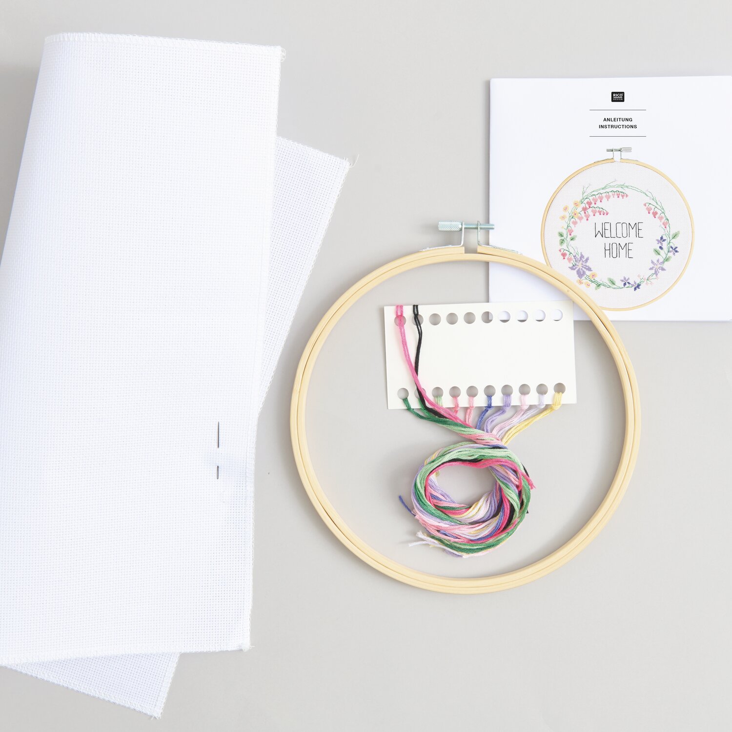 Stickpackung Gezählter Kreuzstich Blumenkranz mit Stickrahmen, Garn und Anleitung auf grauem Hintergrund.