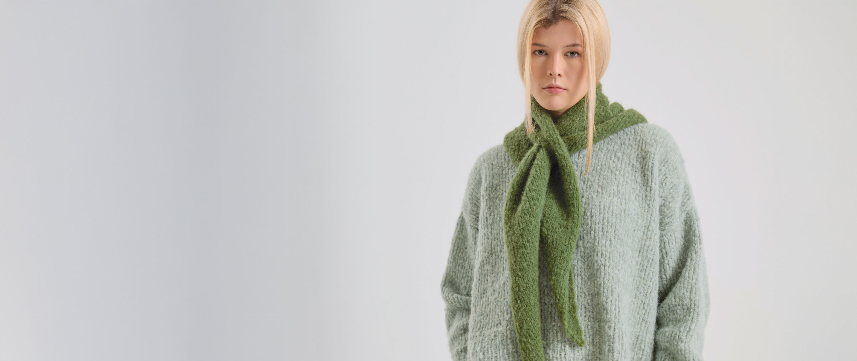 Frau trägt hellgrünen Strickpullover und moosfarbenen Strickschal
