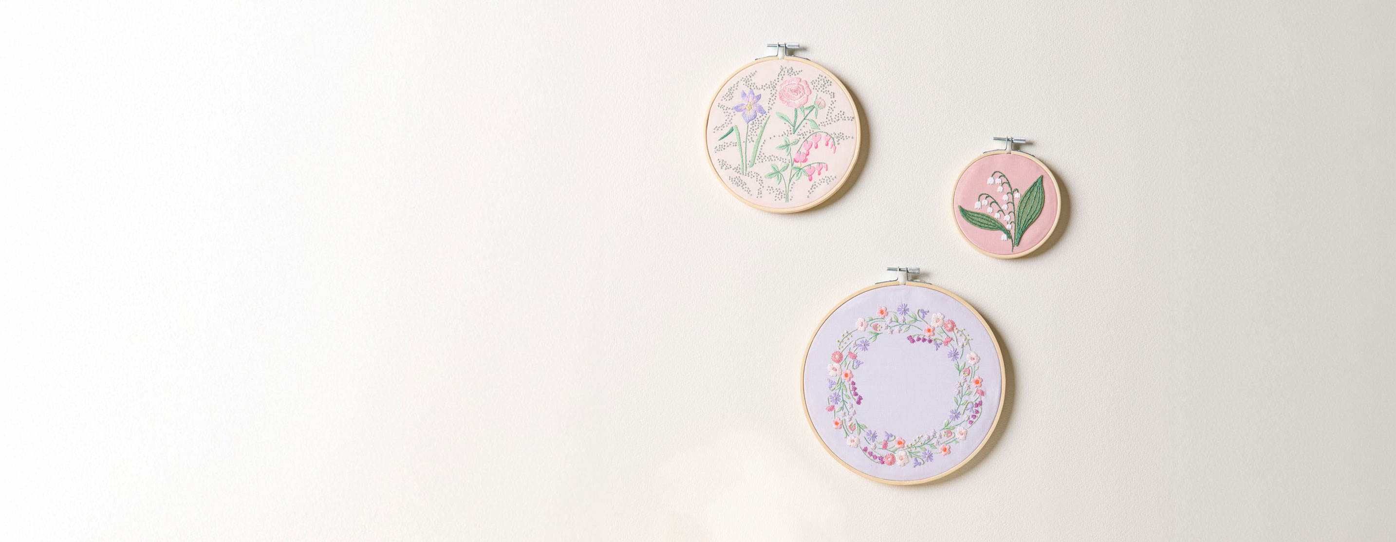 3 Stickringe mit Blumenstickbildern hängen an einer Wand