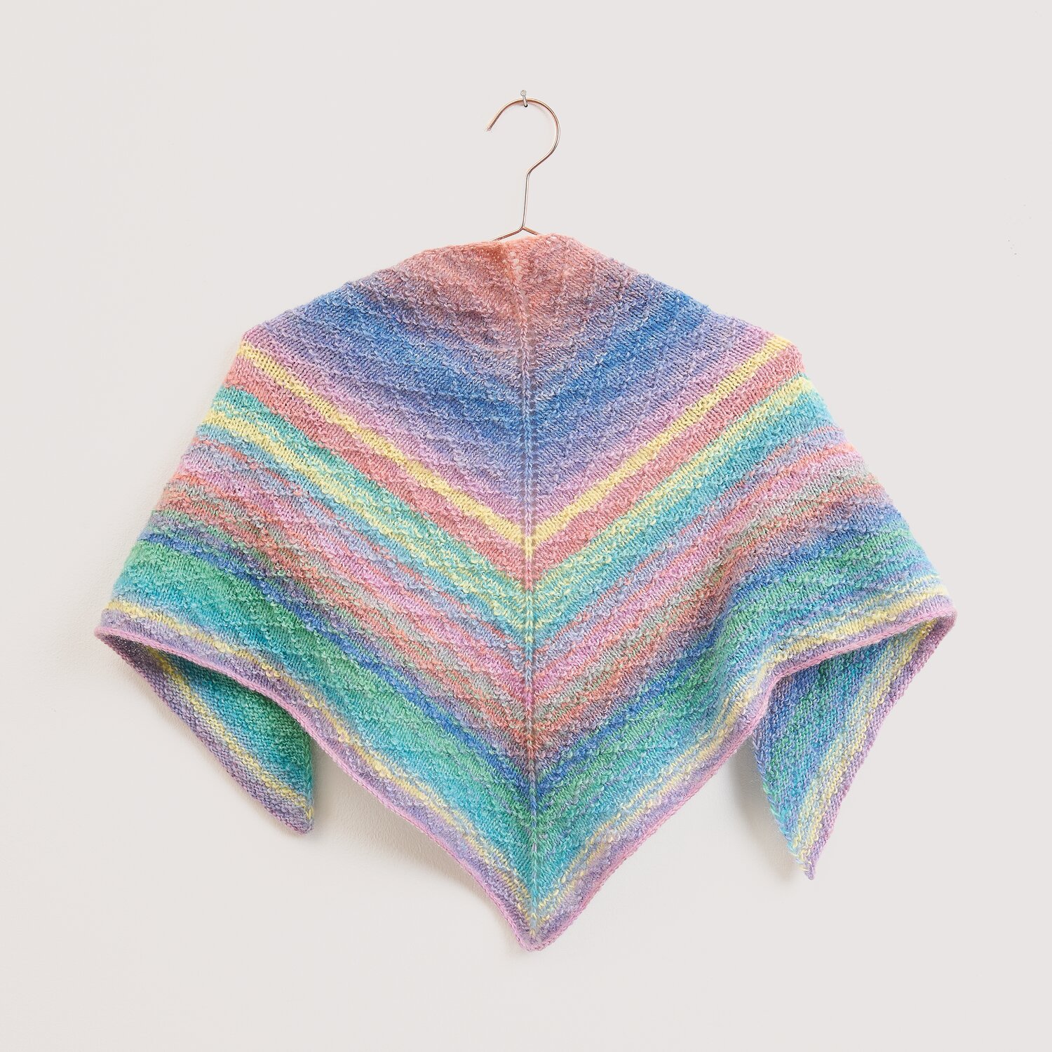 Strickset Mini-Dreieckstuch Modell 11 aus Die Neue Masche No. 16 zeigt ein pastellfarbenes, mehrfarbiges Tuch von Wolle Rödel auf Bügel vor hellem Hintergrund