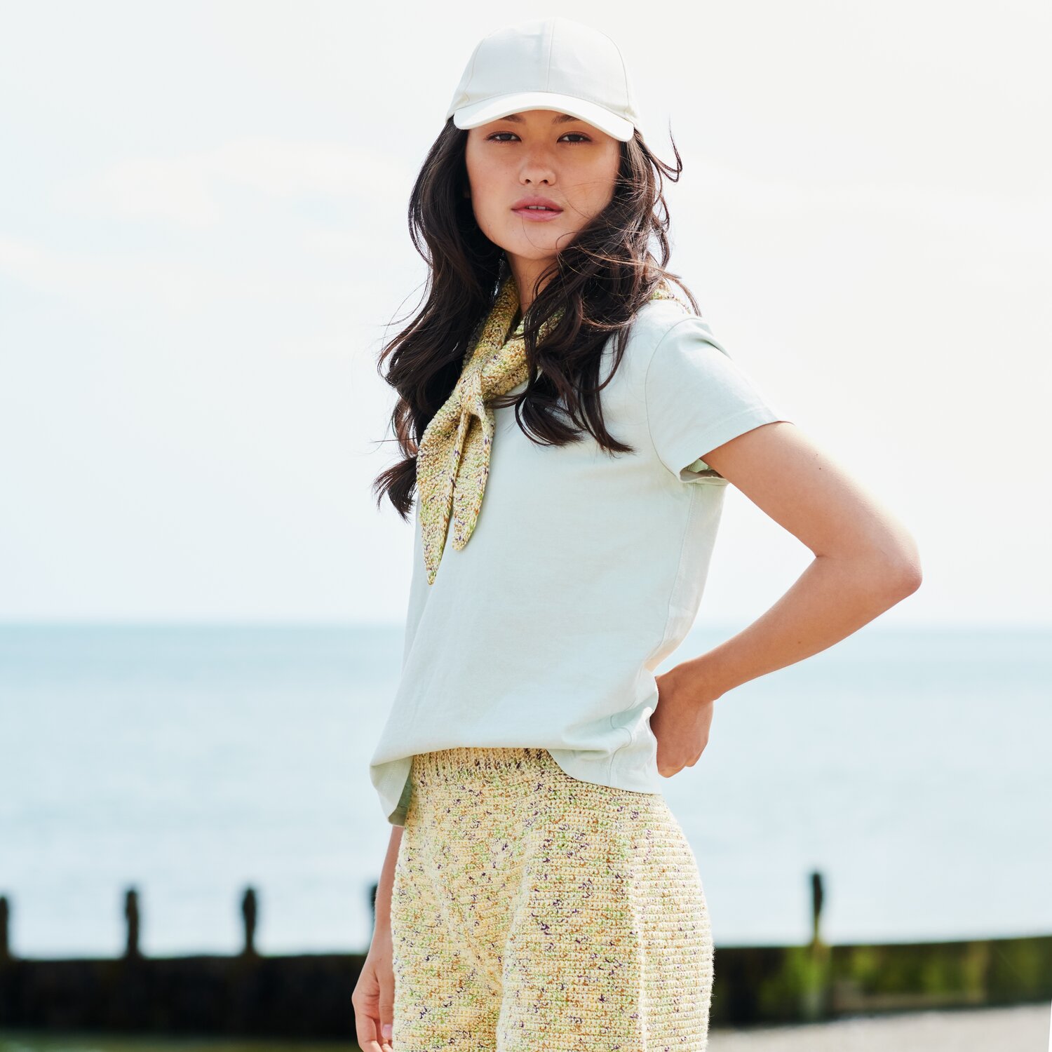 Häkelset Hose Modell 01 aus Lovewool No. 22: Frau am Strand in gelber Häkelhose und weißem T-Shirt.