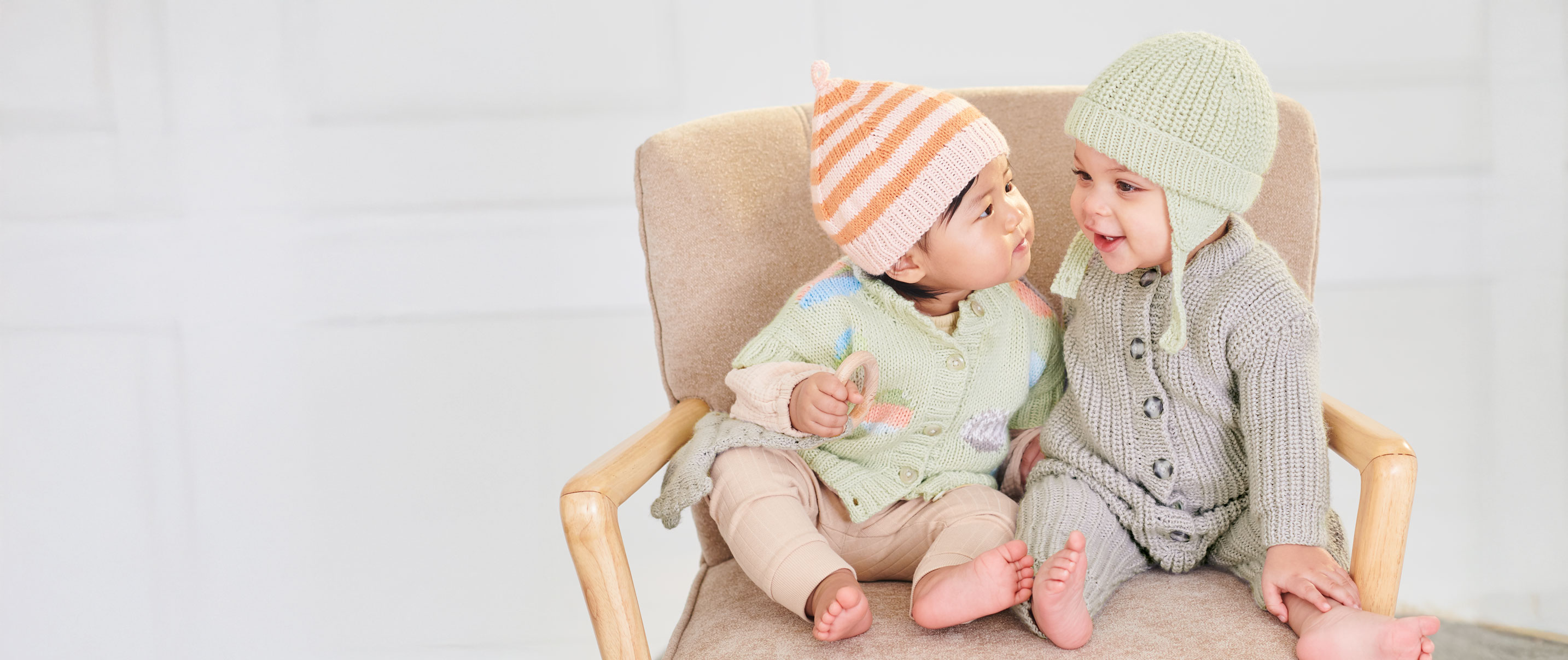 Baby in Strickjacken und Strickmützen sitzen auf einem Sessel