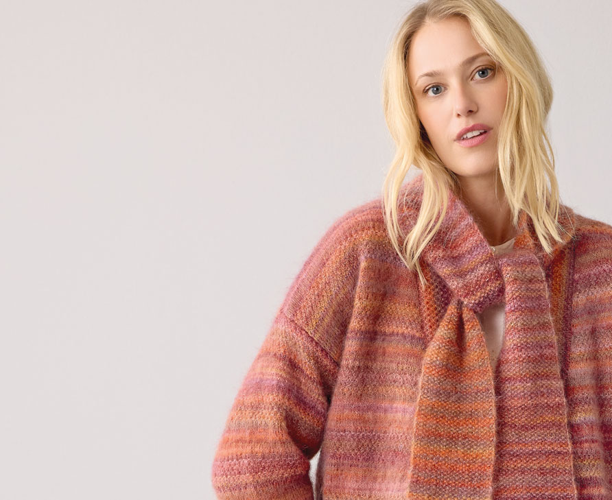 Frau trägt orange gestreiften Strickschal und Strickjacke vor hellem Hintergrund