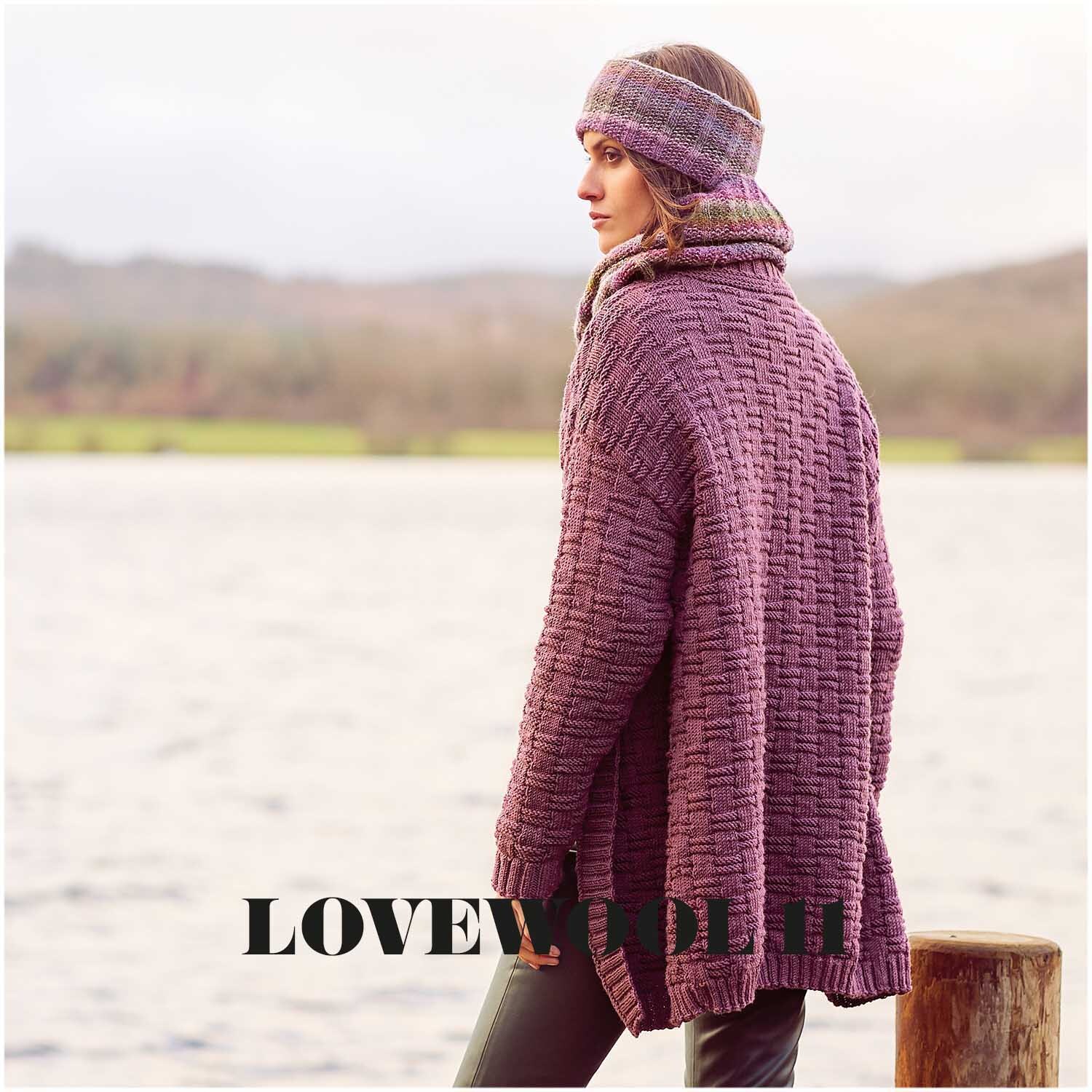 Essentials Merino dk: Frau in gestricktem magentafarbenem Cardigan und Stirnband am Seeufer.