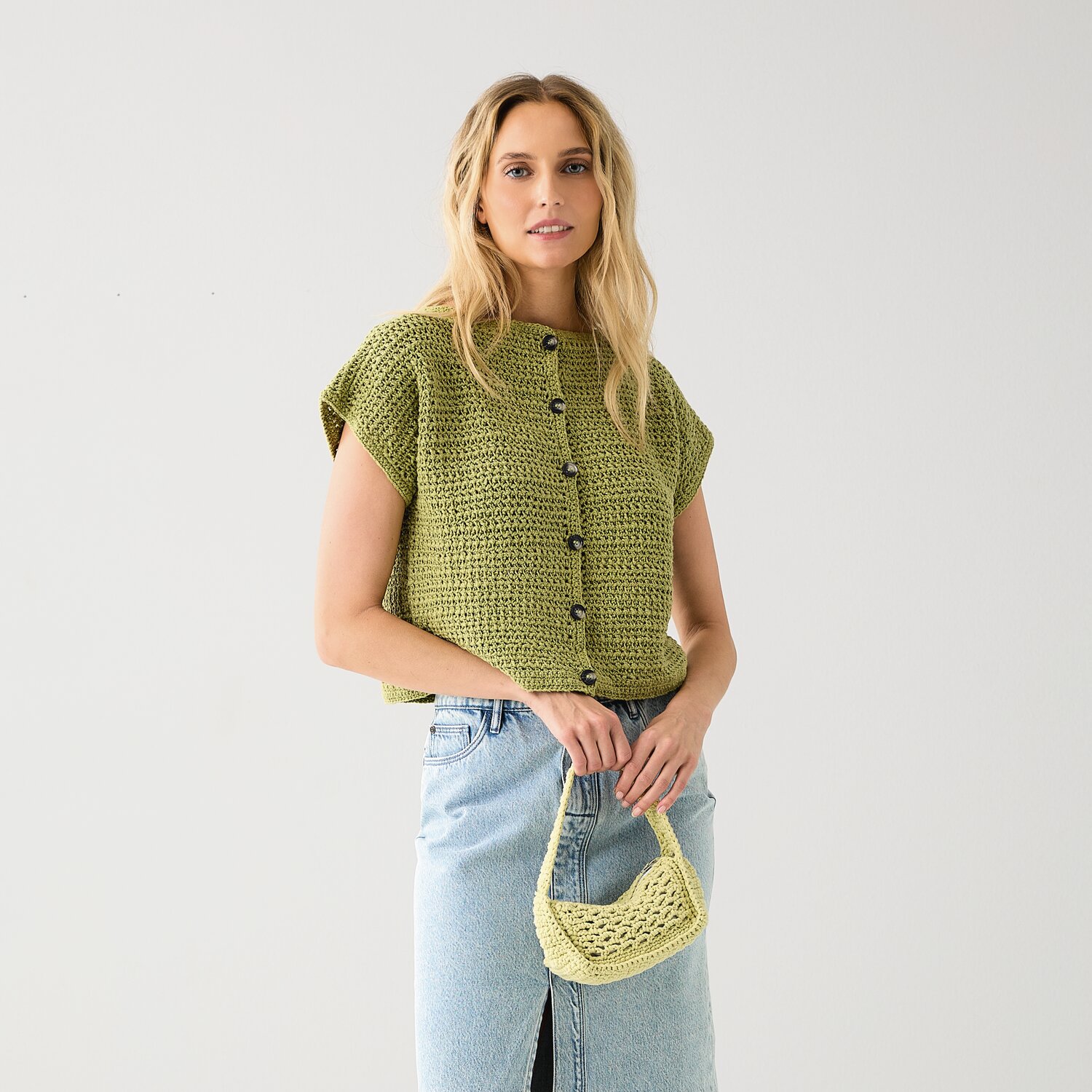 Häkelset Weste Modell 10 aus Die Neue Masche No. 15: Frau trägt grüne Häkelweste und Mini-Häkeltasche, kombiniert mit blauer Jeans.