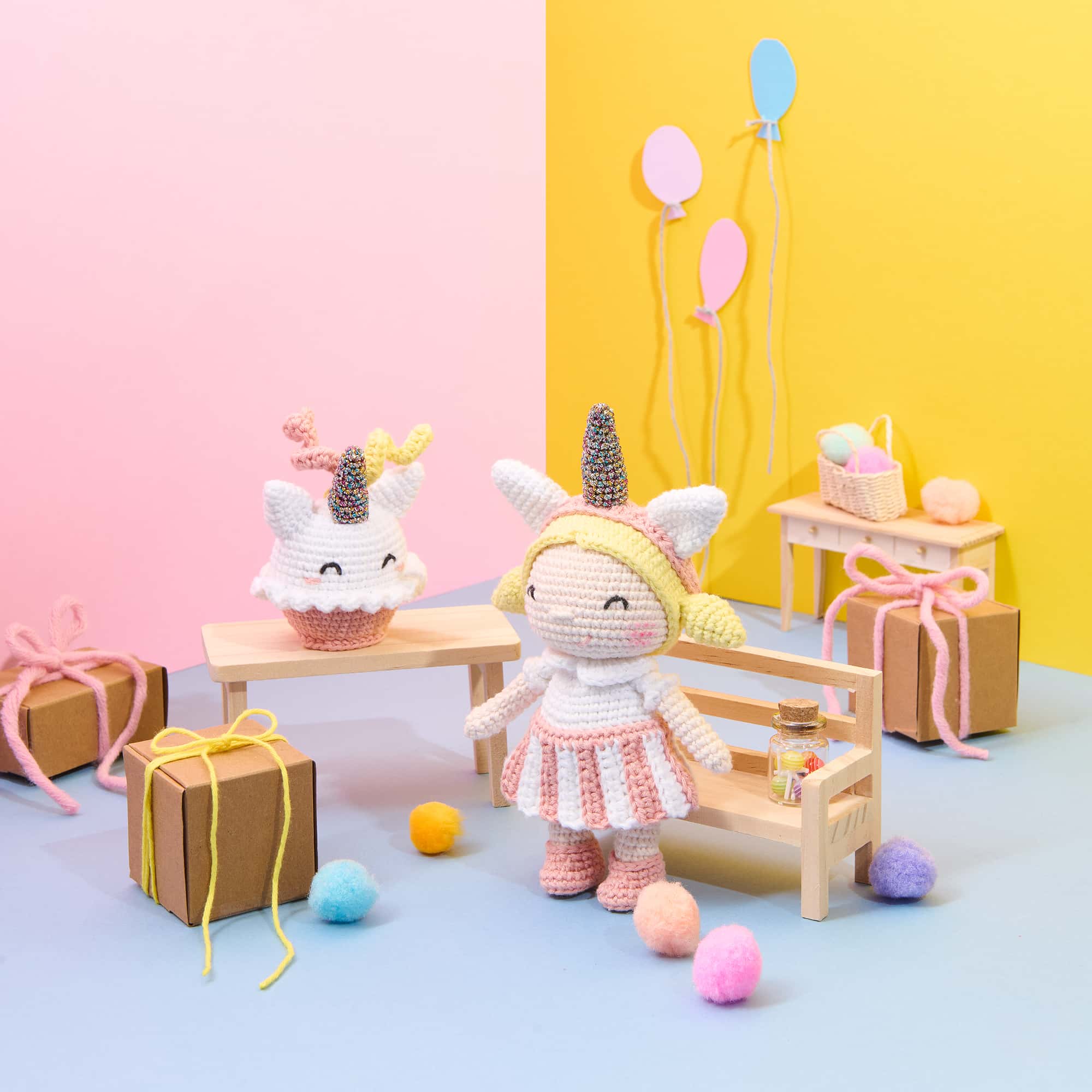 Eine gehäkelte Figur mit Einhorn-Haarreif und ein Cupcake mit Einhorn-Dekoration sind in einer bunt dekorierten Szene mit Partydekoration arrangiert.