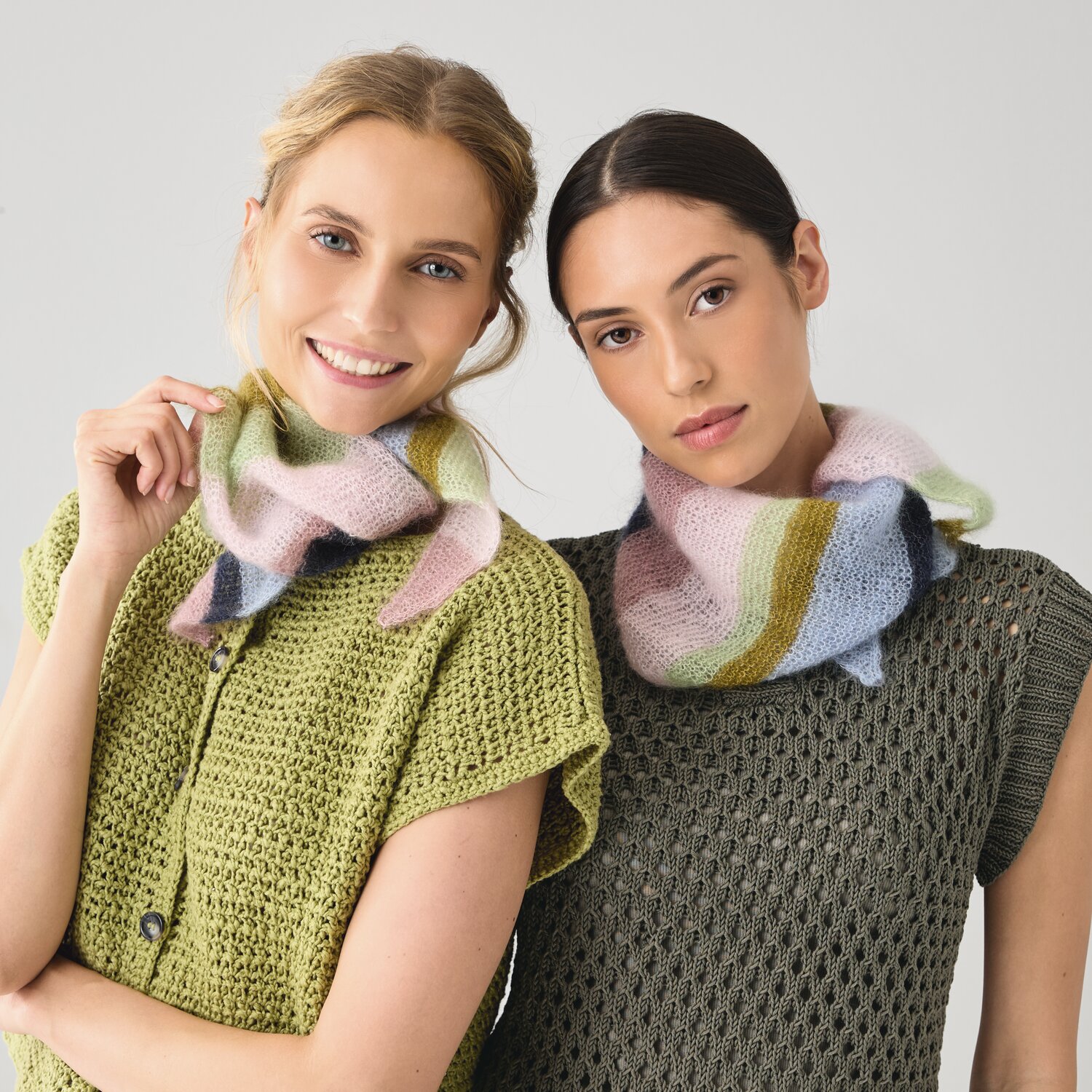 Strickset Dreieckstuch Modell 12 A: Zwei Frauen tragen bunte, gestrickte Schals über grünen Oberteilen.