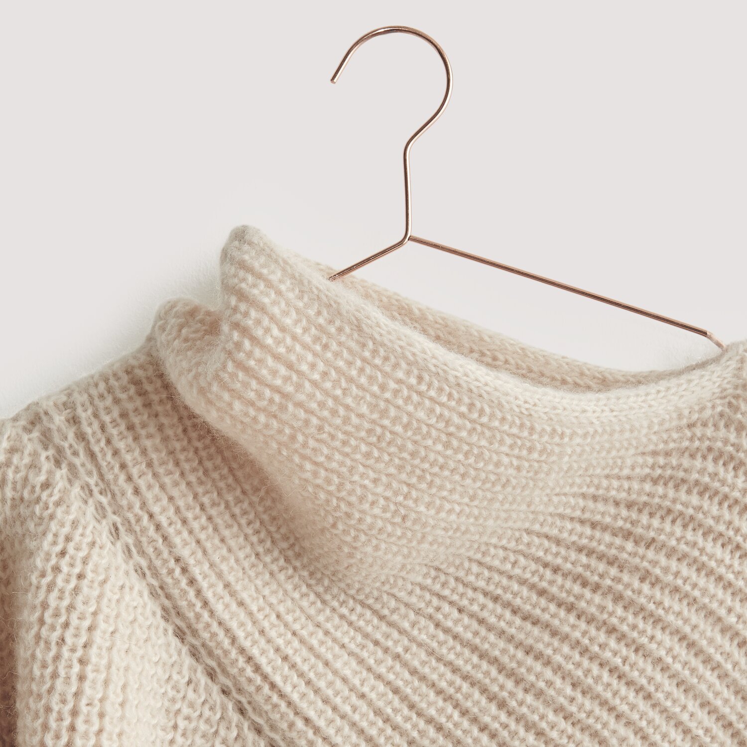 Luxury Merino Alpaca Dream aran: Cremefarbener Strickpullover aus natürlichen Fasern auf Kupferbügel.