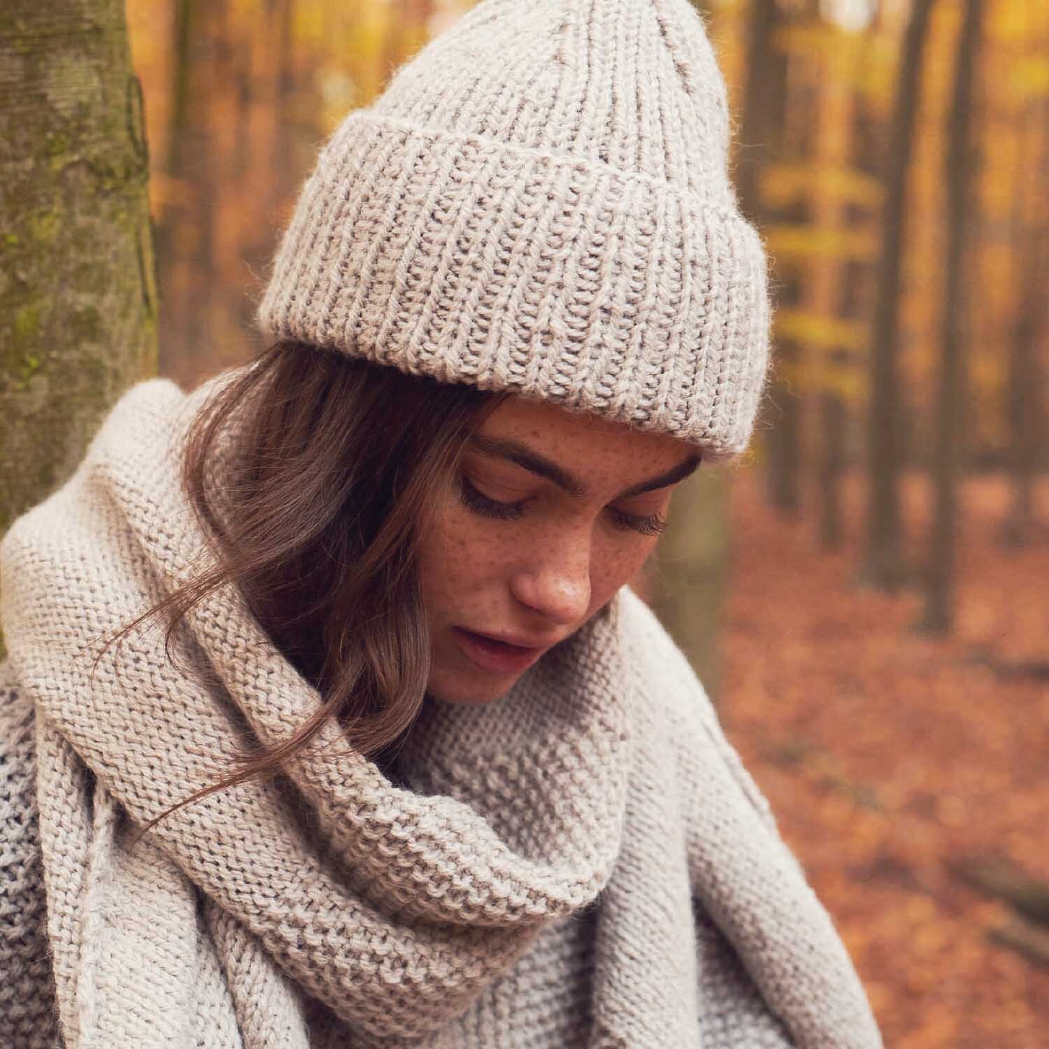 Essentials Alpaca Twist Chunky: Frau im Herbstwald mit gestricktem Schal und Mütze in Silbergrau. Ideal für kühle Tage.