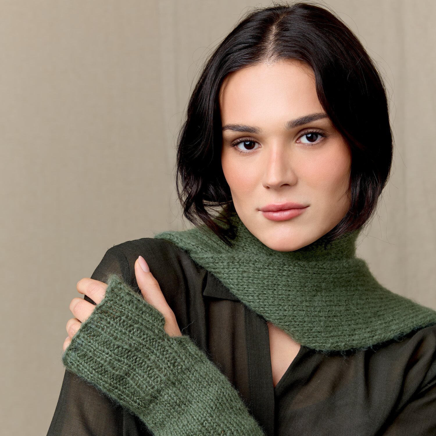Strickset Stulpen Modell 06 aus Luxury Knits Little Pieces, weiche, lang geschnittene Schal- und Stulpen-Kombination in gedecktem Grünton, getragen über transparenter Bluse