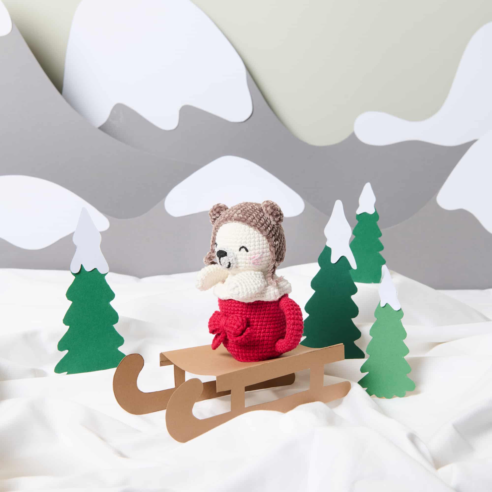 Gehäkelter Seehund sitzt in roter Tasse umgeben von einer Winter-Landschaft.