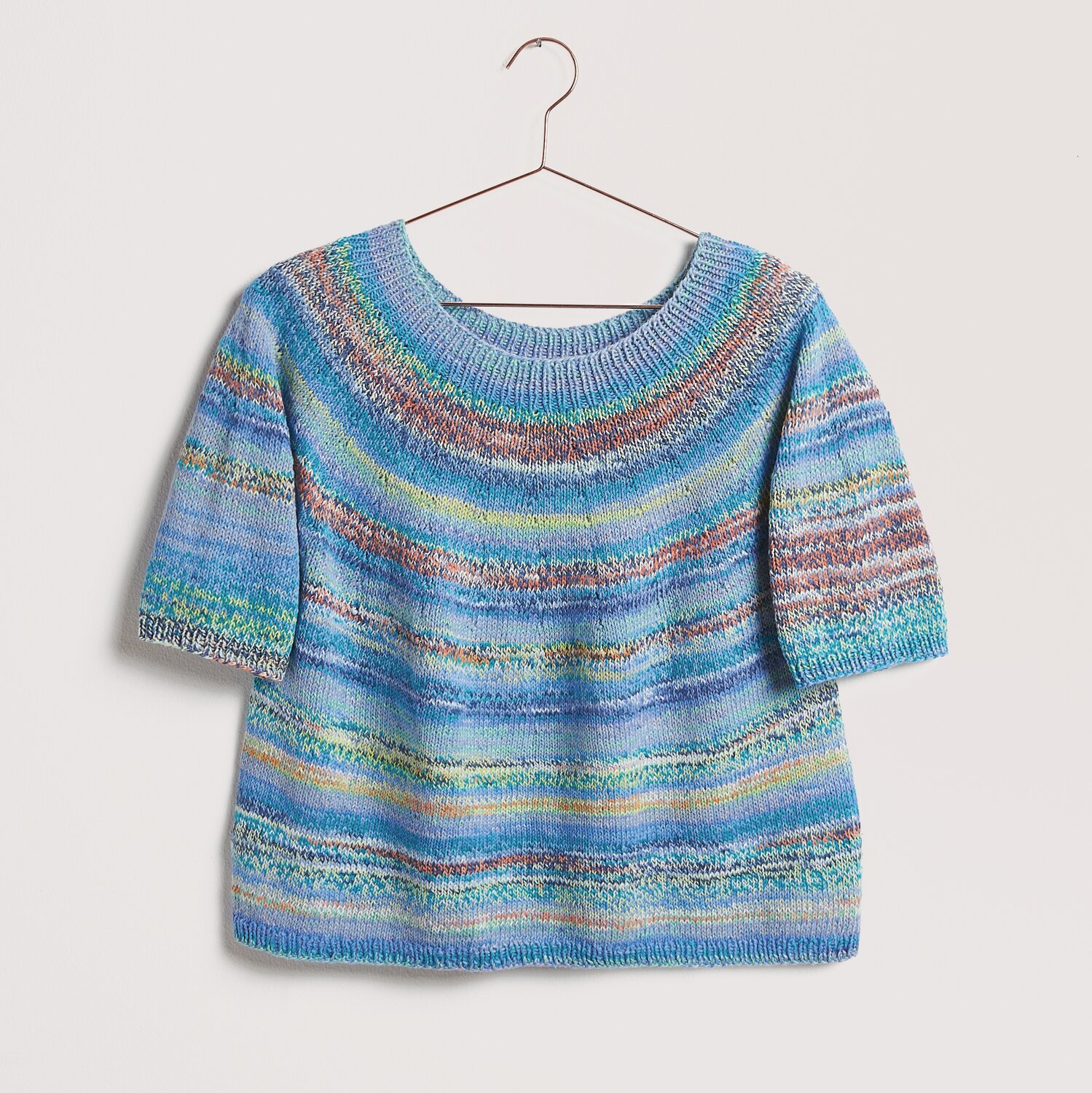Strickset Shirt Modell 22 aus Die Neue Masche No. 12 von idee. Creativmarkt Strickset Shirt Modell 22 aus Die Neue Masche No. 12, blau gestreift, auf einem Kleiderbügel.
