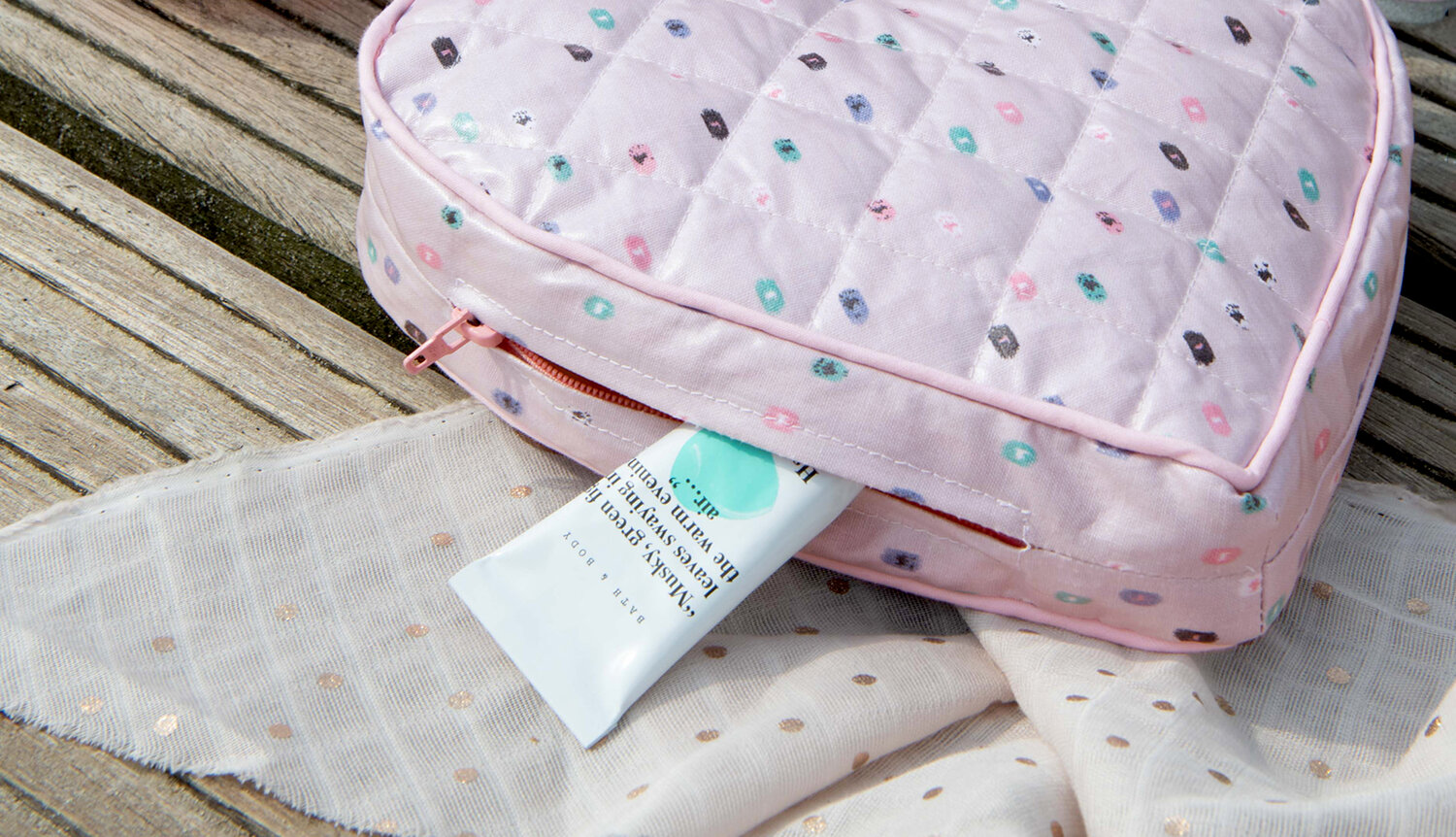 Nähanleitung Clutch in Herzform: Rosa Tasche mit buntem Muster auf Holzbank, daneben ein weißes Tuch.