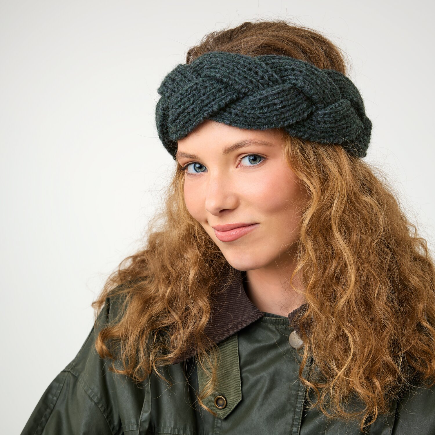 Strickset Stirnband Modell 16a aus Die Neue Masche No. 16, geflochtenes, dunkles Strickstirnband auf jungem Model mit lockigem Haar und olivgrüner Jacke