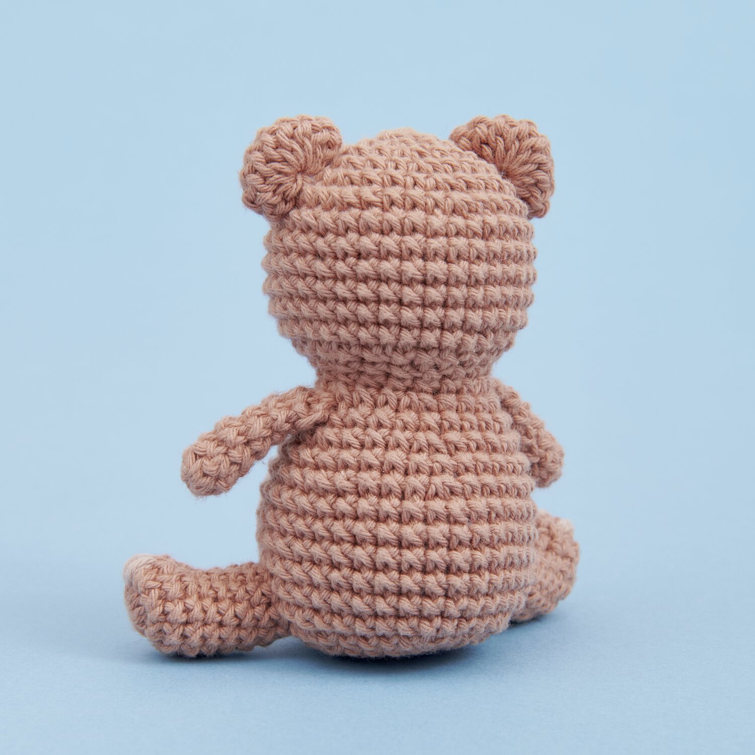 Ricorumi Mini Easy Häkelset - Teddy: Rückansicht eines gehäkelten Teddys in Beige auf blauem Hintergrund.