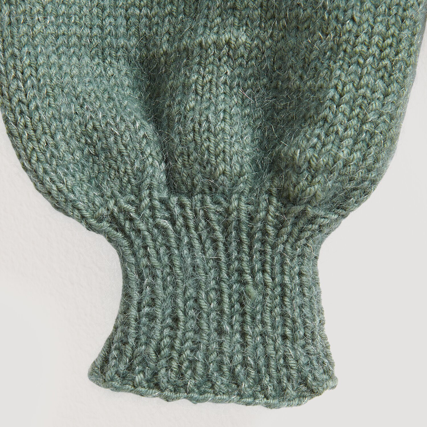 Essentials Merino dk: Nahaufnahme eines gestrickten Ärmels in Efeu-Grün, weiche Textur.