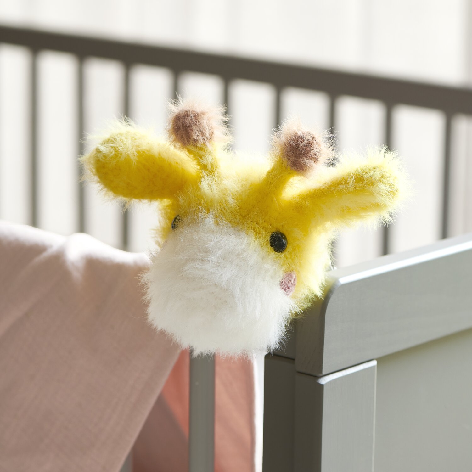 Ricorumi Furry Animals: Gelbe und weiße gestrickte Giraffe mit schwarzen Sicherheitsaugen am Kinderbett.