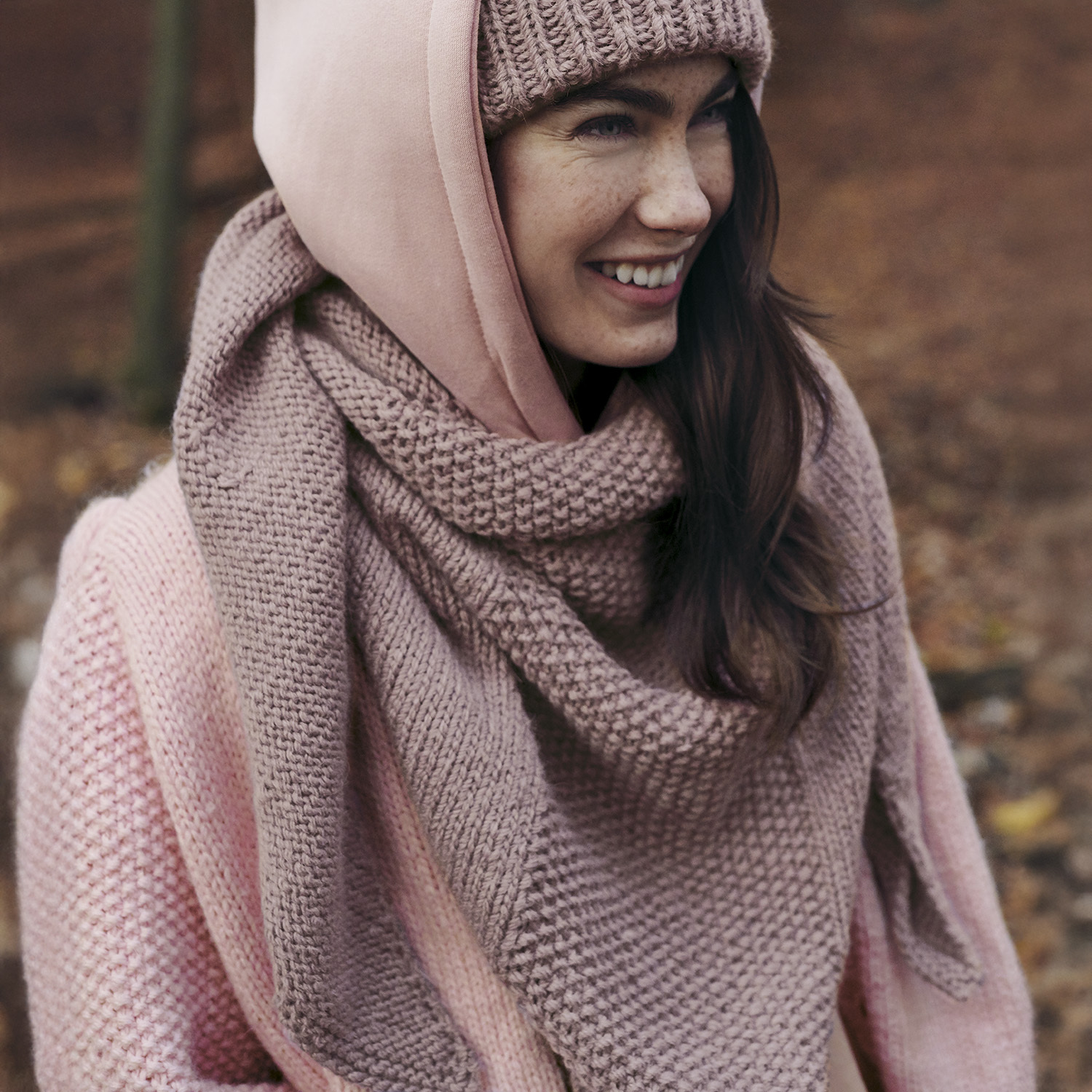 Strickanleitung Dreieckstuch aus Essentials Alpaca Twist chunky: Frau trägt rosa Strickset aus Schal, Mütze und Pullover im Herbstwald.