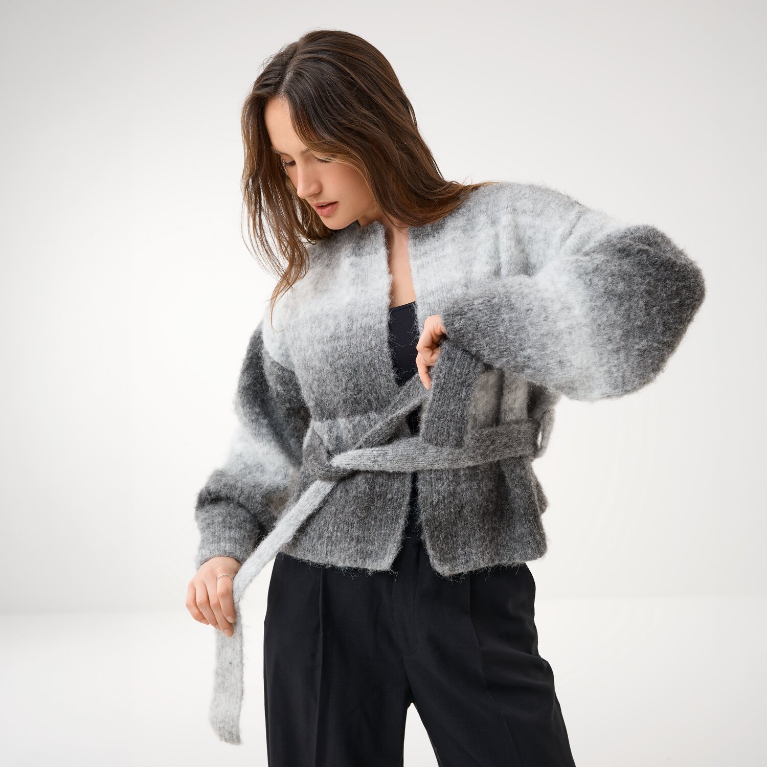 Strickset Jacke Modell 05 aus Die Neue Masche No. 16, locker geschnittene, flauschige Wickeljacke mit Bindegürtel, von Frau zu schwarzer Hose getragen