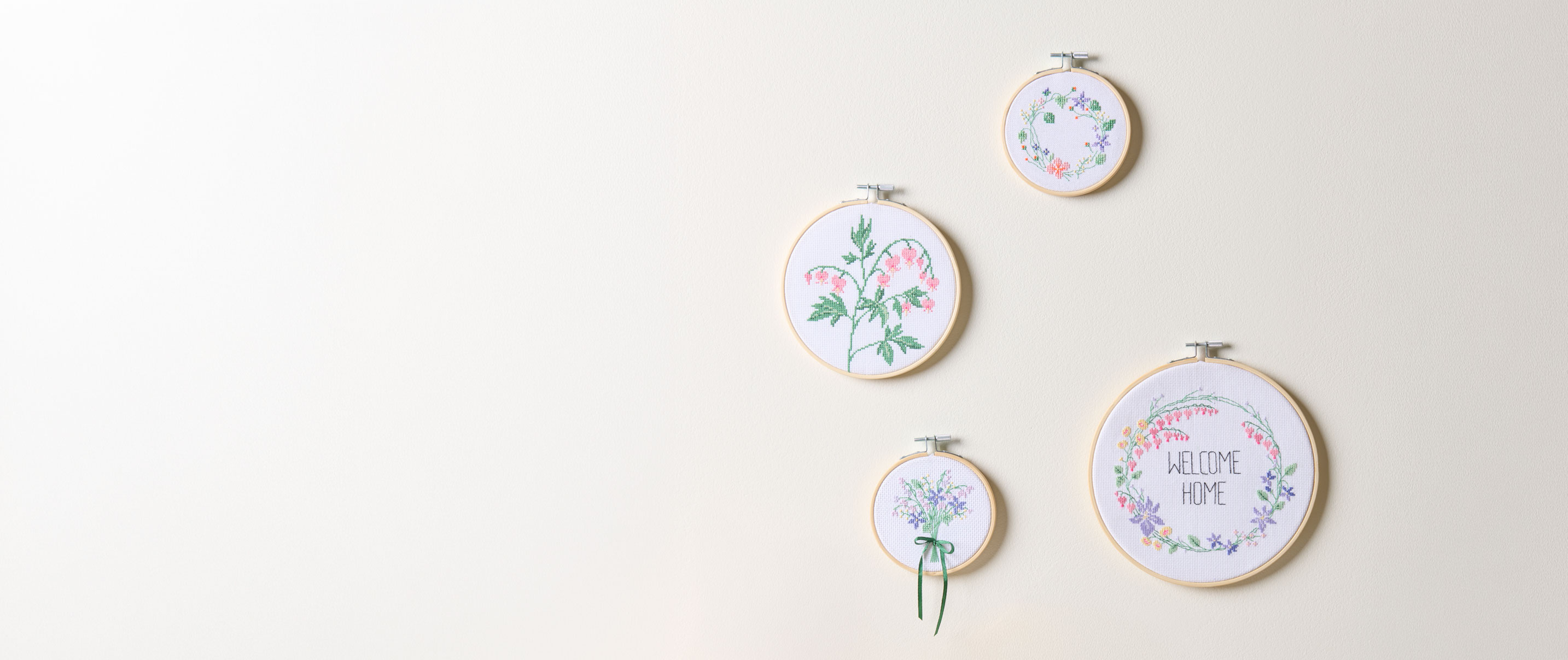 4 blumige Stickbilder im Stickrahmen hängen an einer Wand