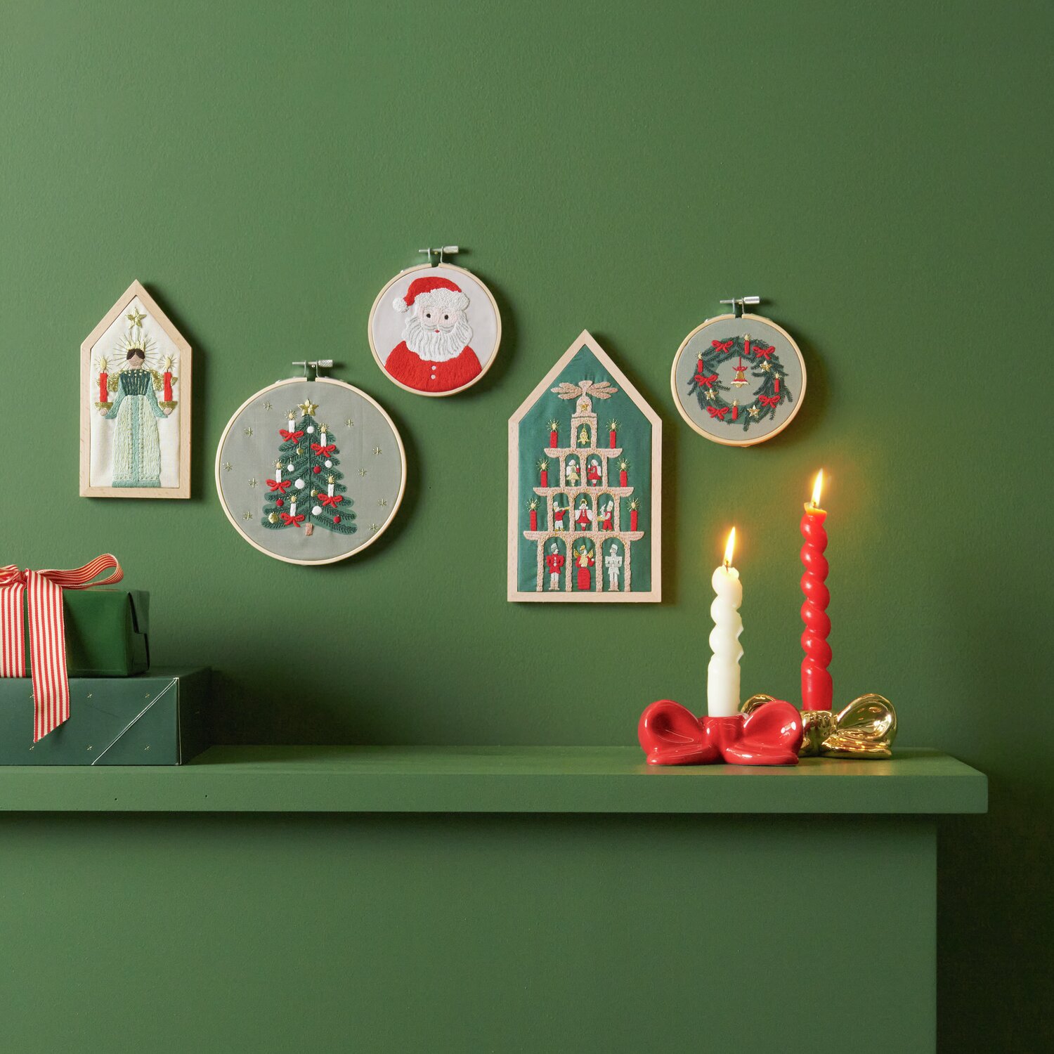 Stickpackung Weihnachtskranz vorgezeichnet: Fünf weihnachtliche Stickbilder an grüner Wand, darunter Kerzen und Geschenke.