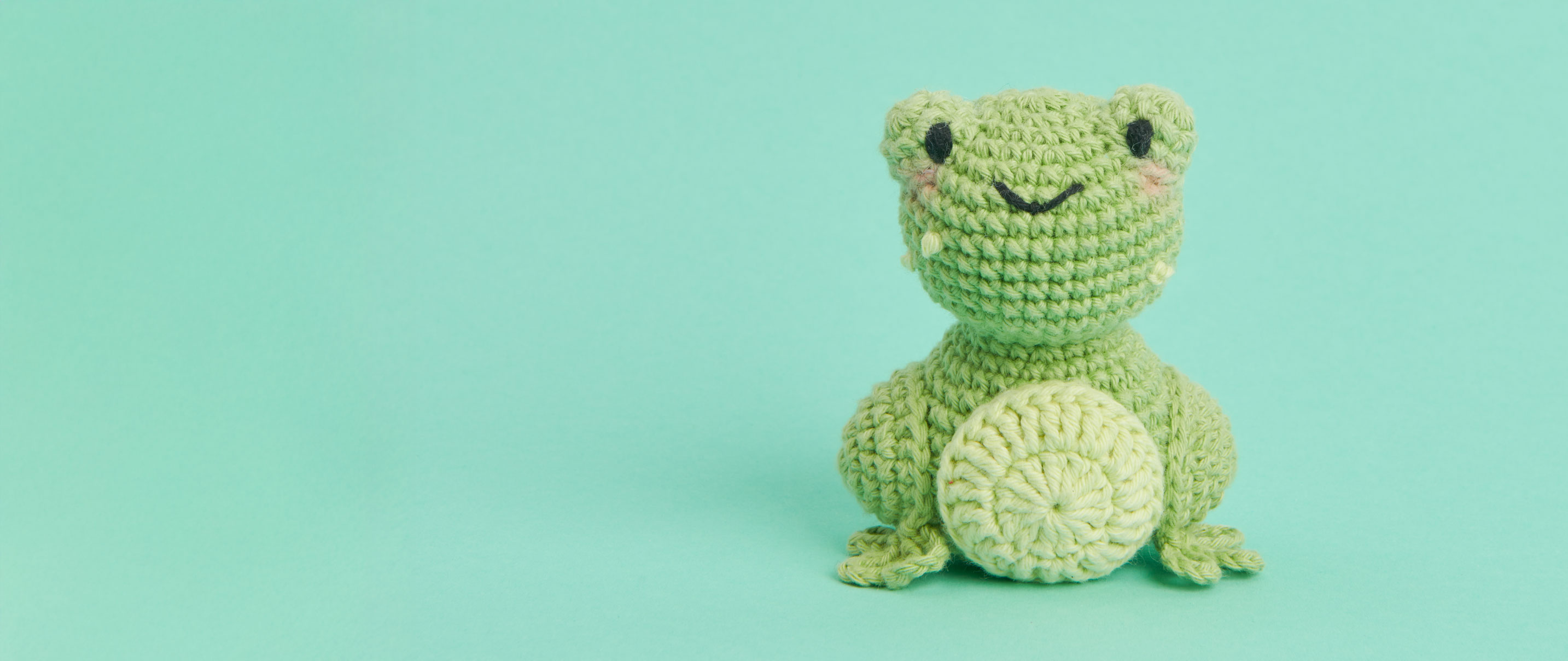 Gehäkelter Frosch sitzt vor grünem Hintergrund