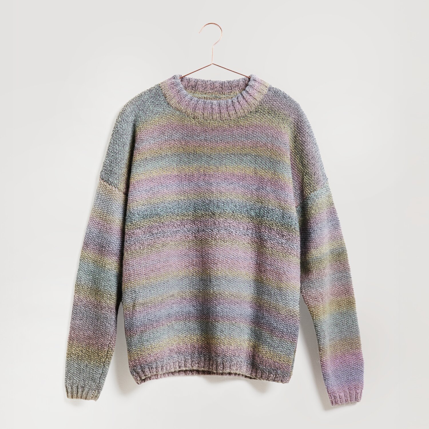 Ein gestrickter Pullover in sanften Pastelltönen hängt an einem Kleiderbügel. Der Pullover zeigt ein Streifenmuster in Blau, Rosa und Grün. Marke: Modell Legeware. Perfekt für einen gemütlichen Look.