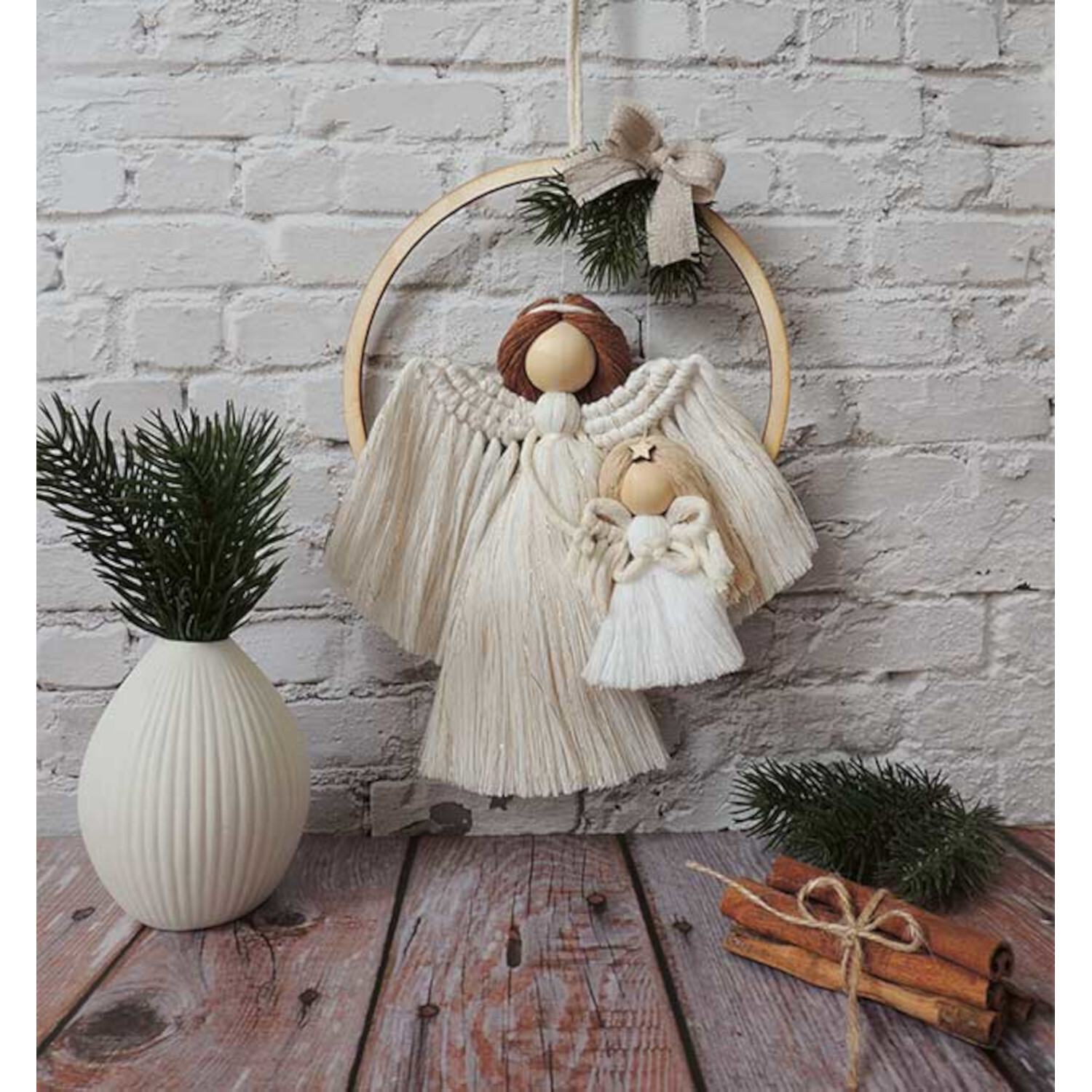 Märchenhafte Makramee Engel vor einer Ziegelwand, dekoriert mit Tannenzweigen und Zimtstangen.