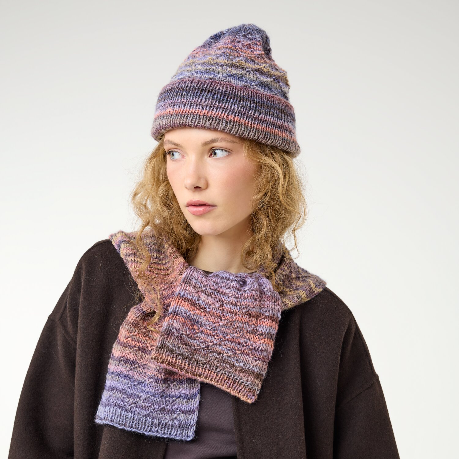 Strickset Minischal + Mütze Modell 24 aus Die Neue Masche No. 16, gestrickt im mehrfarbig melierten Garn, getragen von Frau mit lockigen Haaren und dunklem Mantel