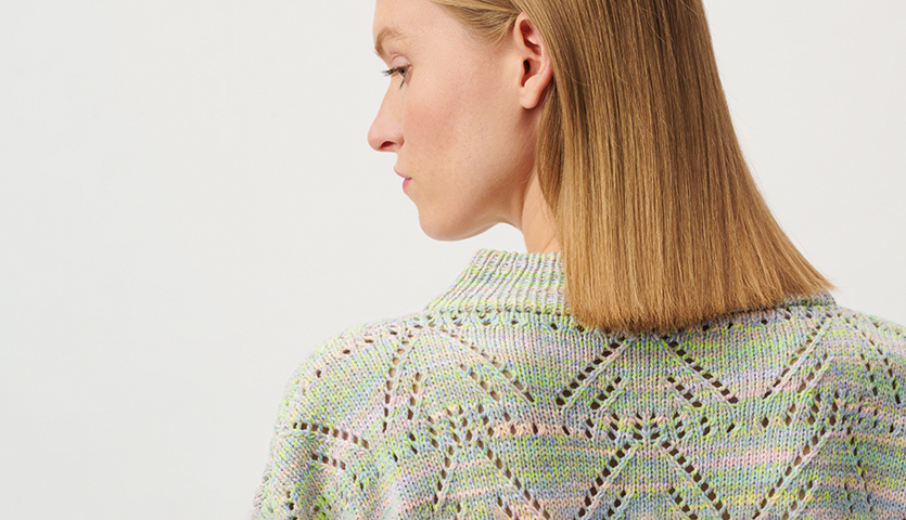 Strickanleitung Pullover aus Creative Summer Sprinkles Strickanleitung Pullover aus Creative Summer Sprinkles: Frau trägt pastellfarbenen Pullover mit Lochmuster, seitlich fotografiert.