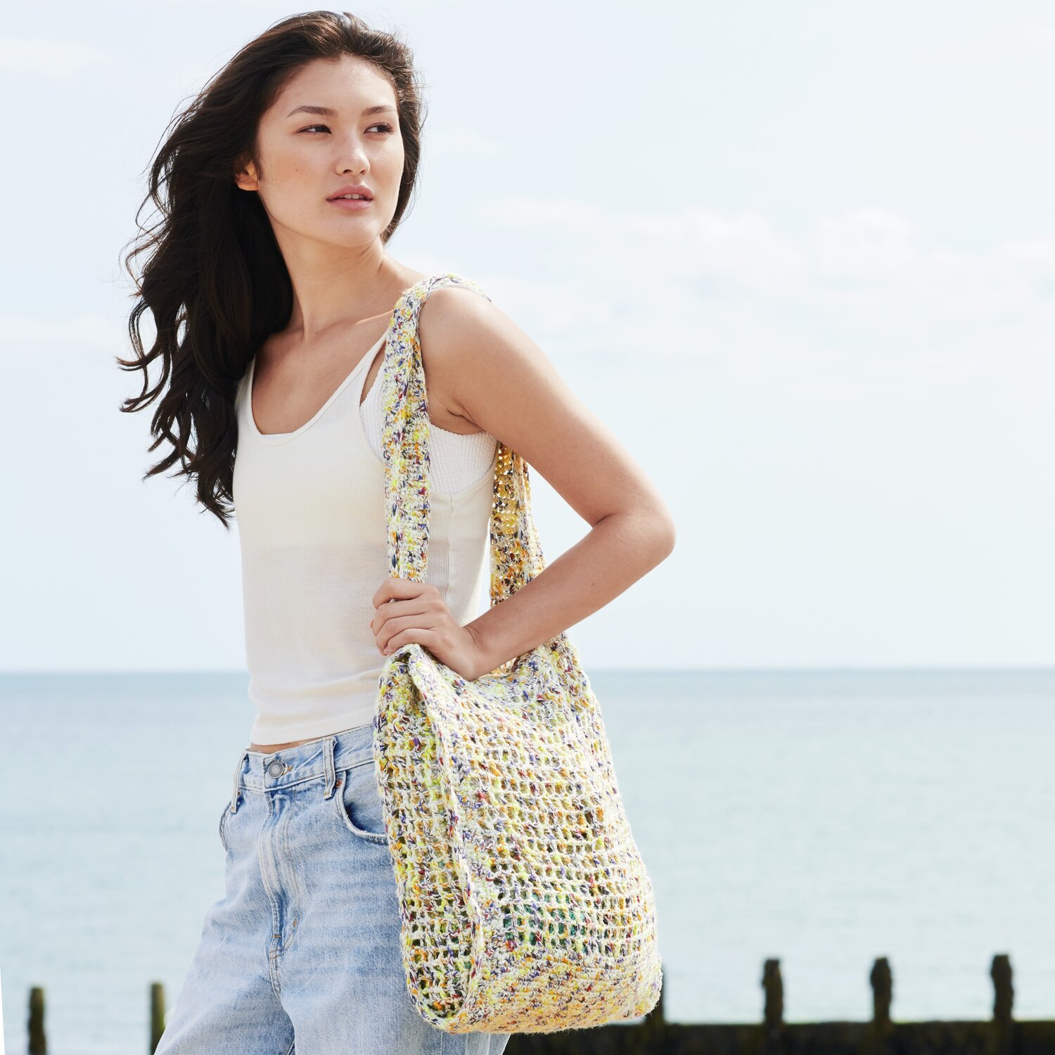 Häkelset Tasche Modell 28 aus Lovewool No. 22: Frau am Strand mit bunter, gehäkelter Tasche.