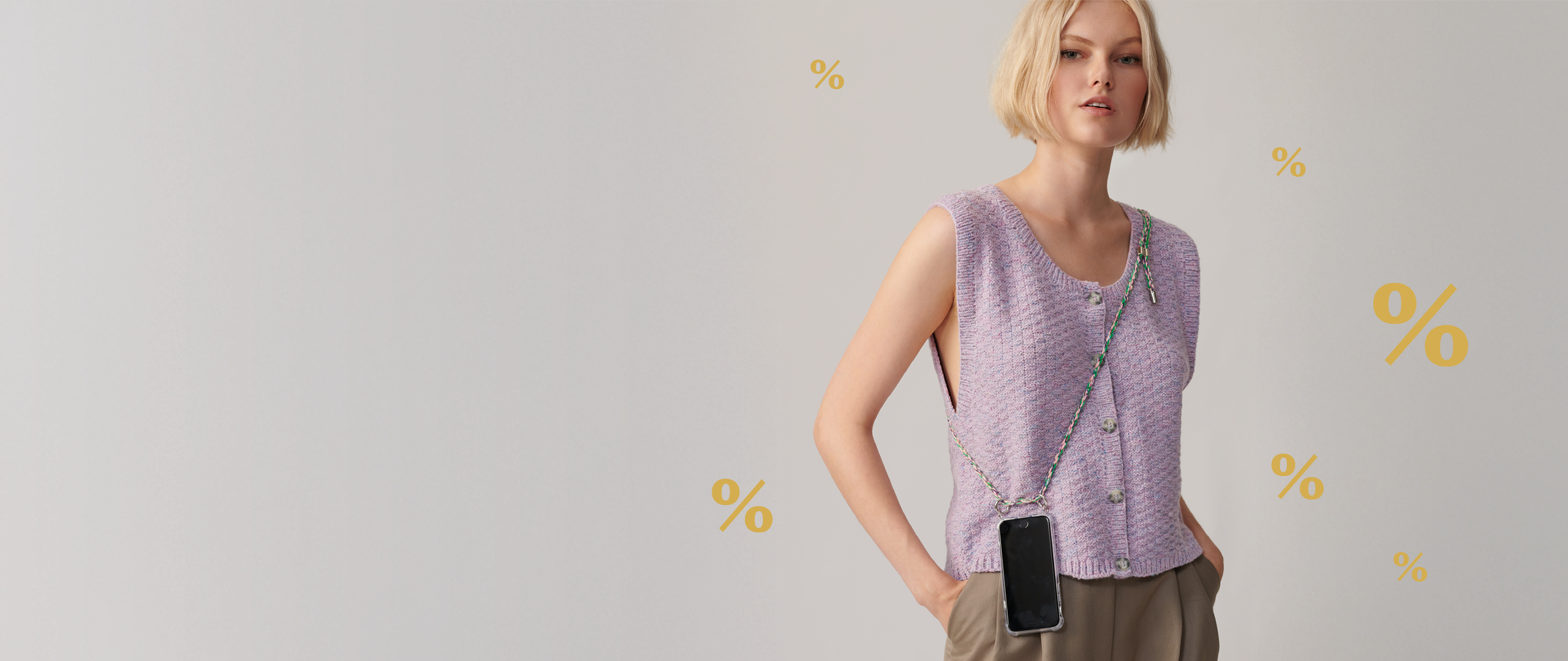 Frau steht mit fliederfarbener Weste vor grauem Hintergrund, goldene % Zeichen