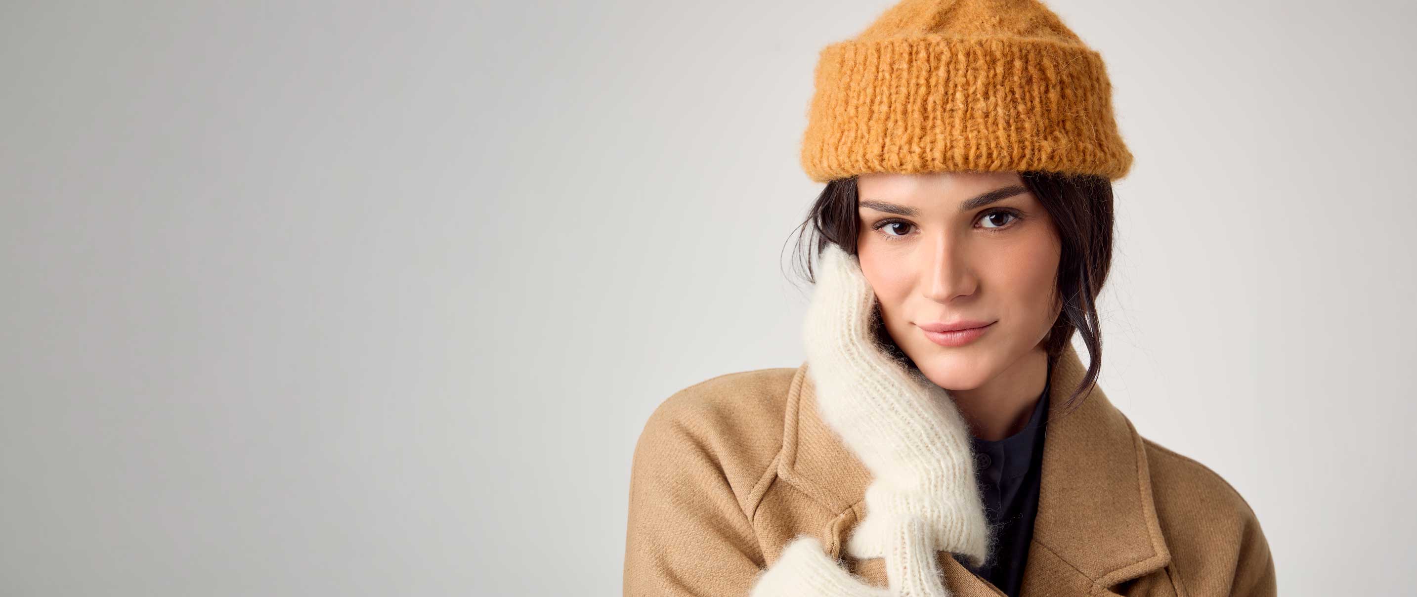 Frau trägt senffarbene Strickmütze und cremefarbene Strickhandschuhe