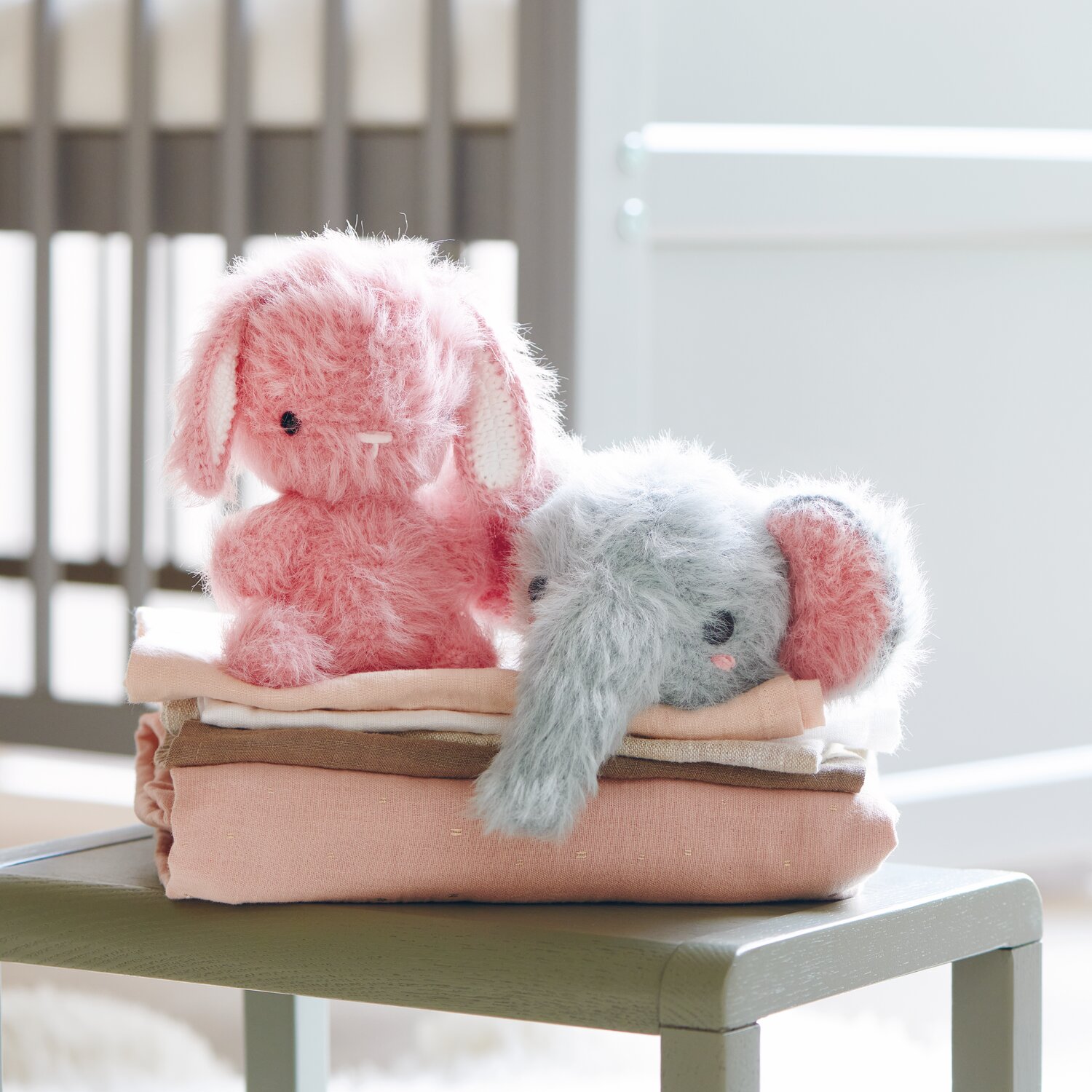Creative Ricorumi dk 25g Farbe Creme von Rico Design Ricorumi Furry Animals: Zwei flauschige Stofftiere, Hase in Pink und Elefant in Patina, auf gefalteten Decken.